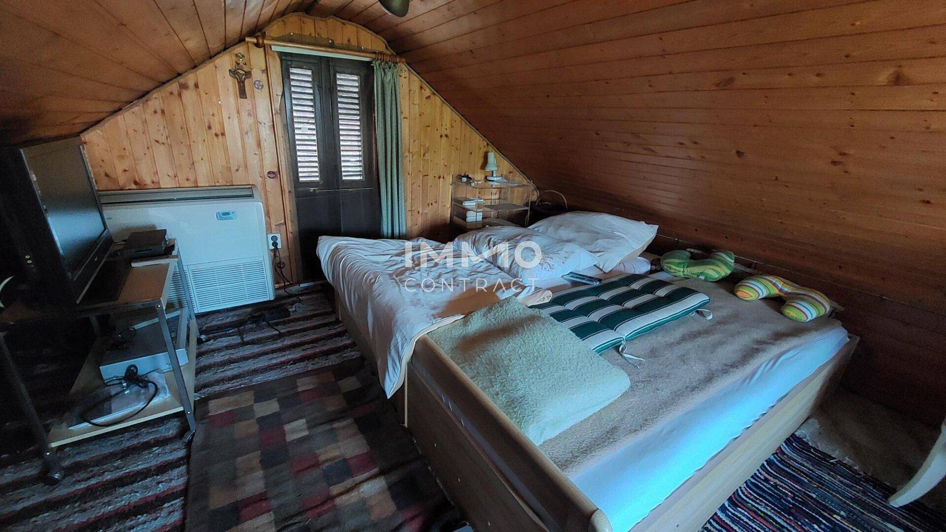 Schlafzimmer im Dachgeschoss mit schrägen Holzdecken, einem Bett und einer Klimaanlage.