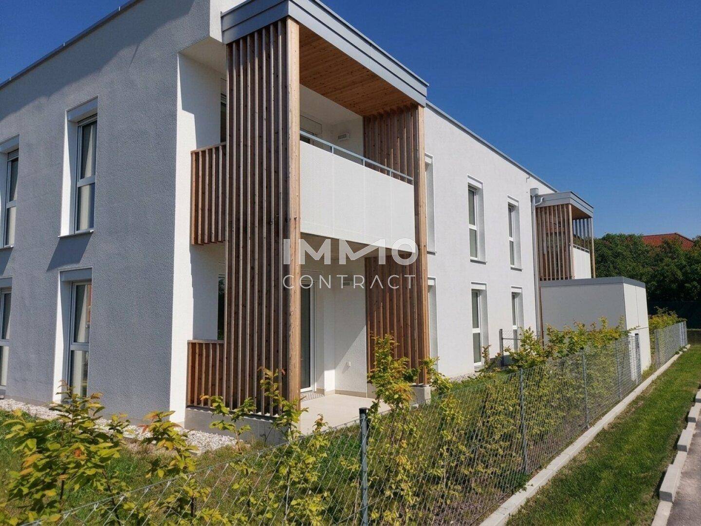 Seitenansicht eines modernen Reihenhauses mit Holzelementen an den Balkonen und gepflegter Bepflanzung.