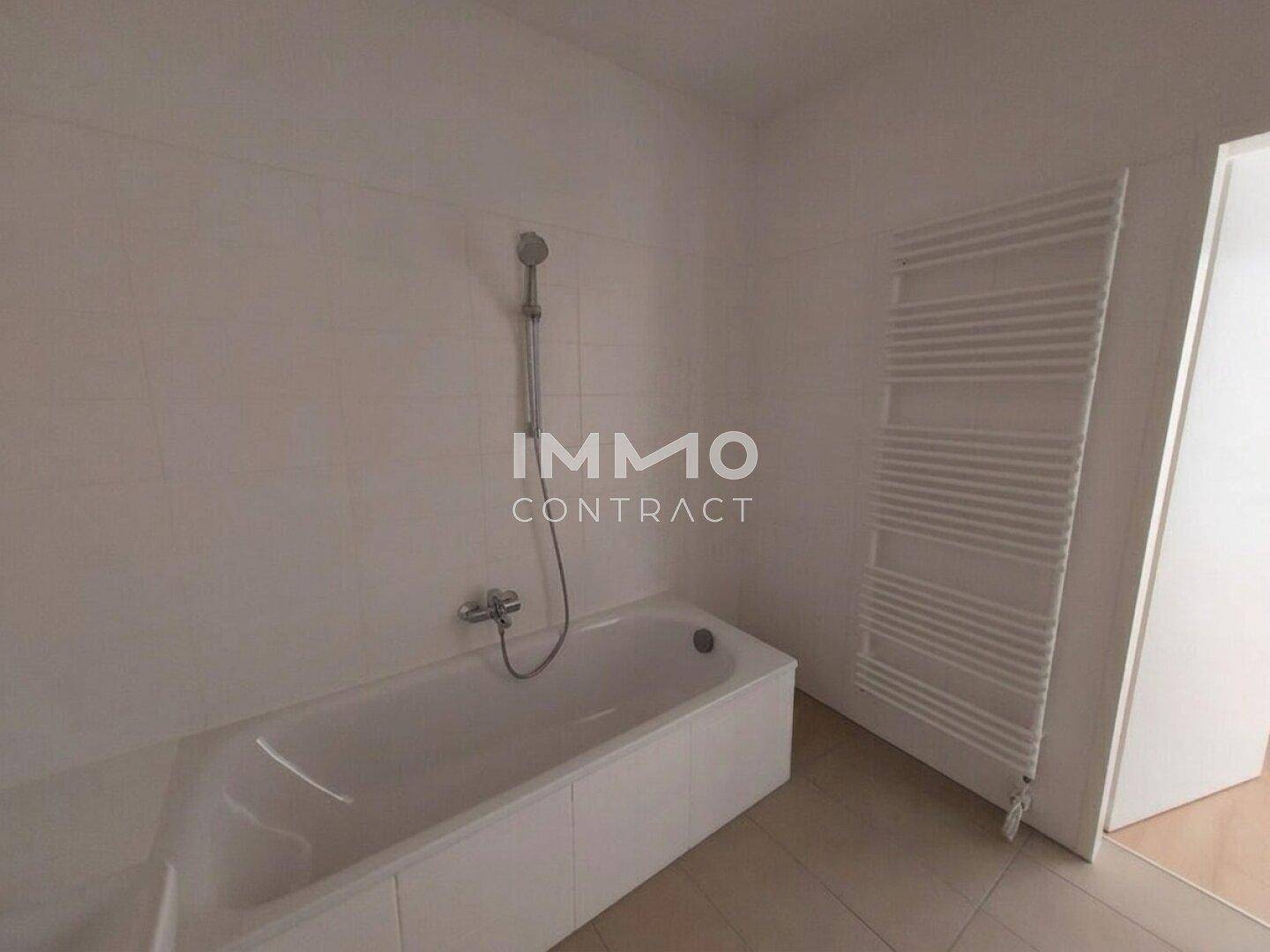 Modernes Badezimmer mit Badewanne und beheiztem Handtuchhalter, in hellen Fliesen gehalten.