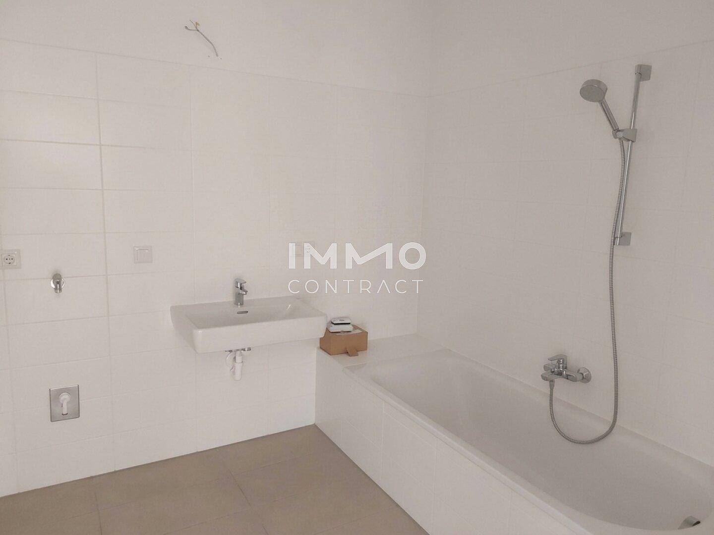 Helles Badezimmer mit Badewanne und Waschbecken, ausgestattet mit weißen Fliesen und moderner Armatur.