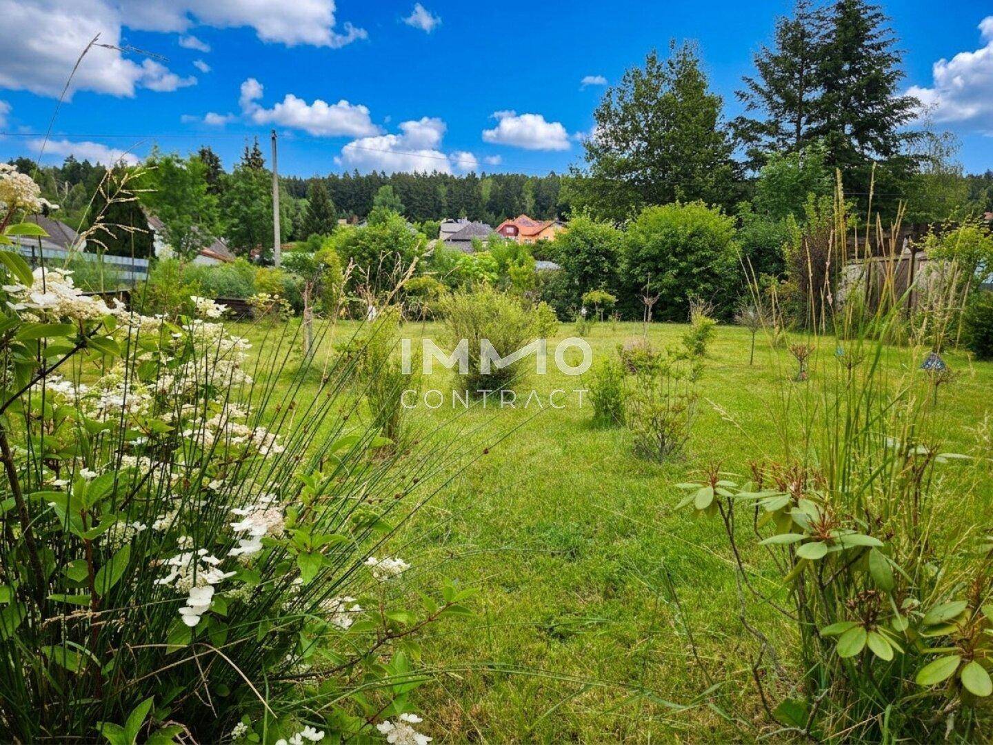 Weitläufiger Garten mit blühenden Sträuchern und Bäumen, umgeben von Natur.