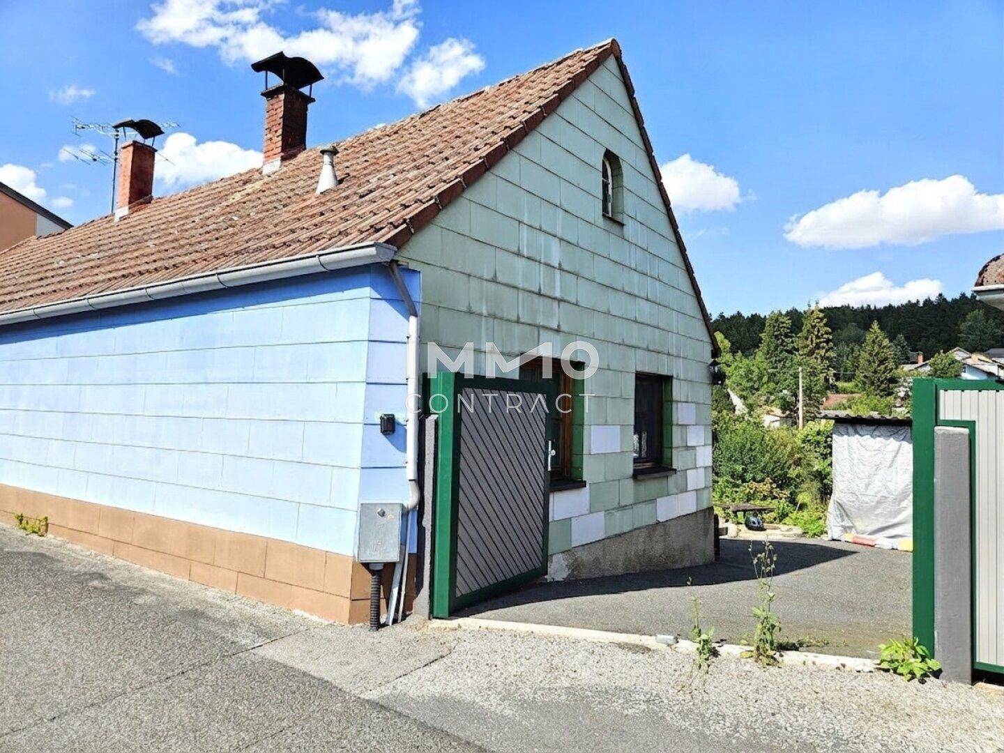 Ansicht des Hauses mit blauer und grüner Fassade, Einfahrt und Gartentor.