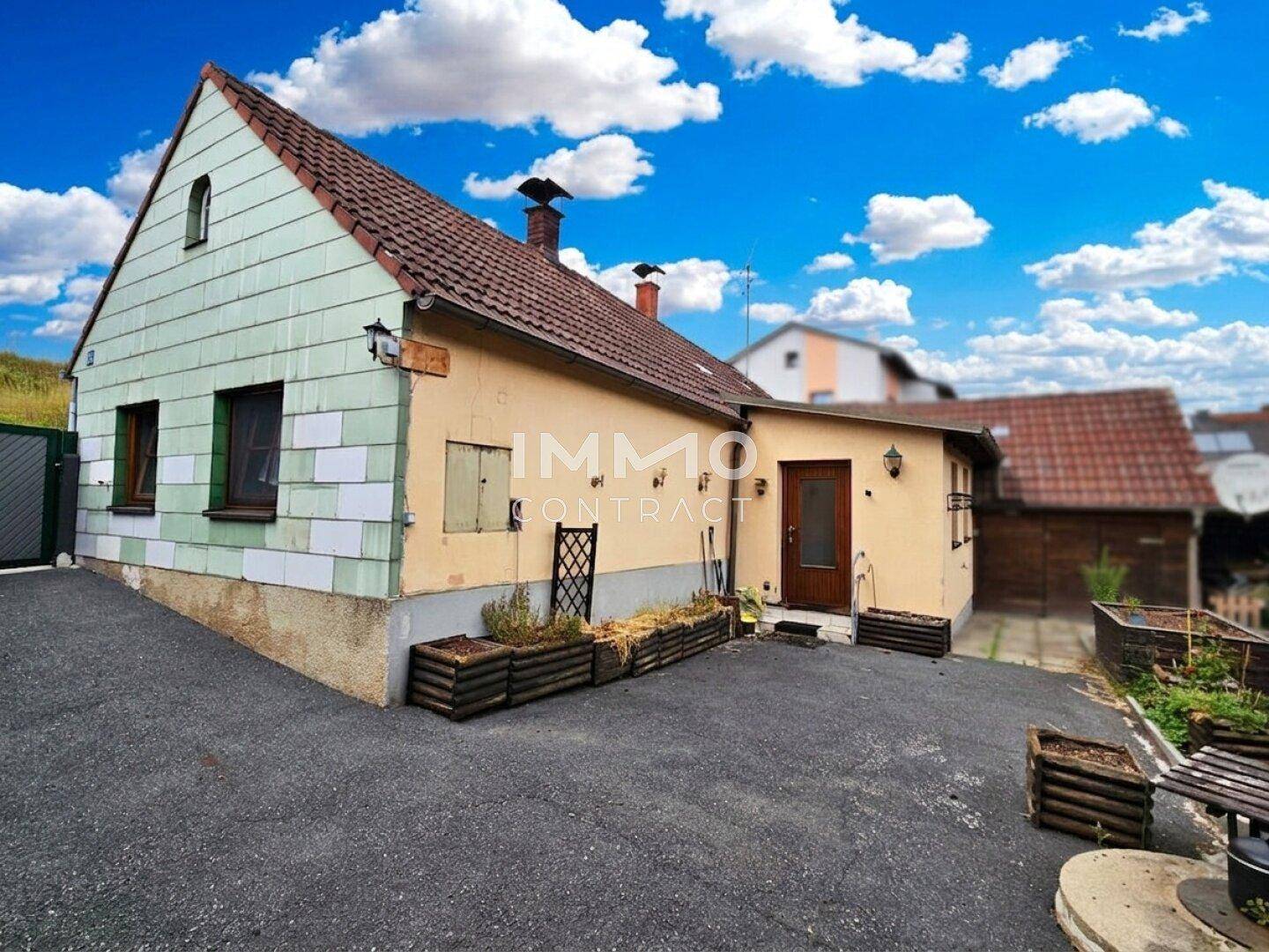 Rückansicht des Hauses mit Anbau, Eingangsbereich und gepflasterter Fläche.