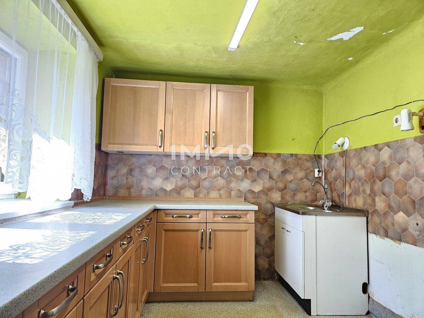 Einfache Küche mit Holzschränken, Spülbecken und gefliestem Arbeitsbereich.