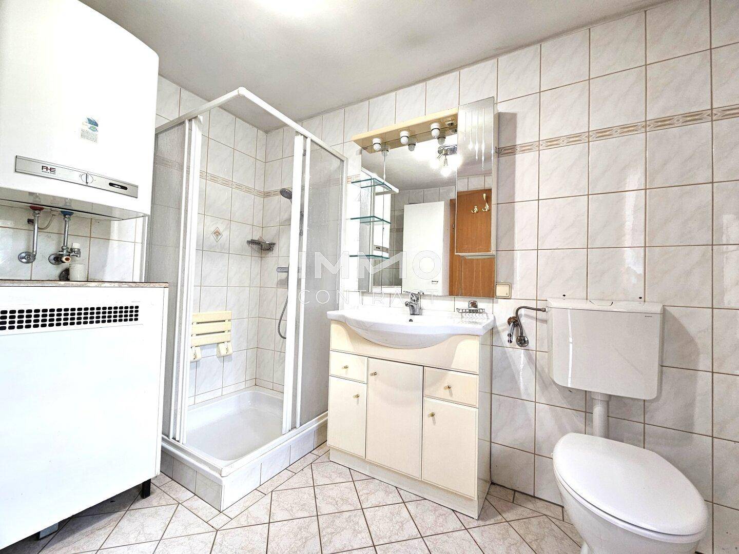 Gefliestes Badezimmer mit Dusche, Waschbecken und Toilette, in hellem Zustand.