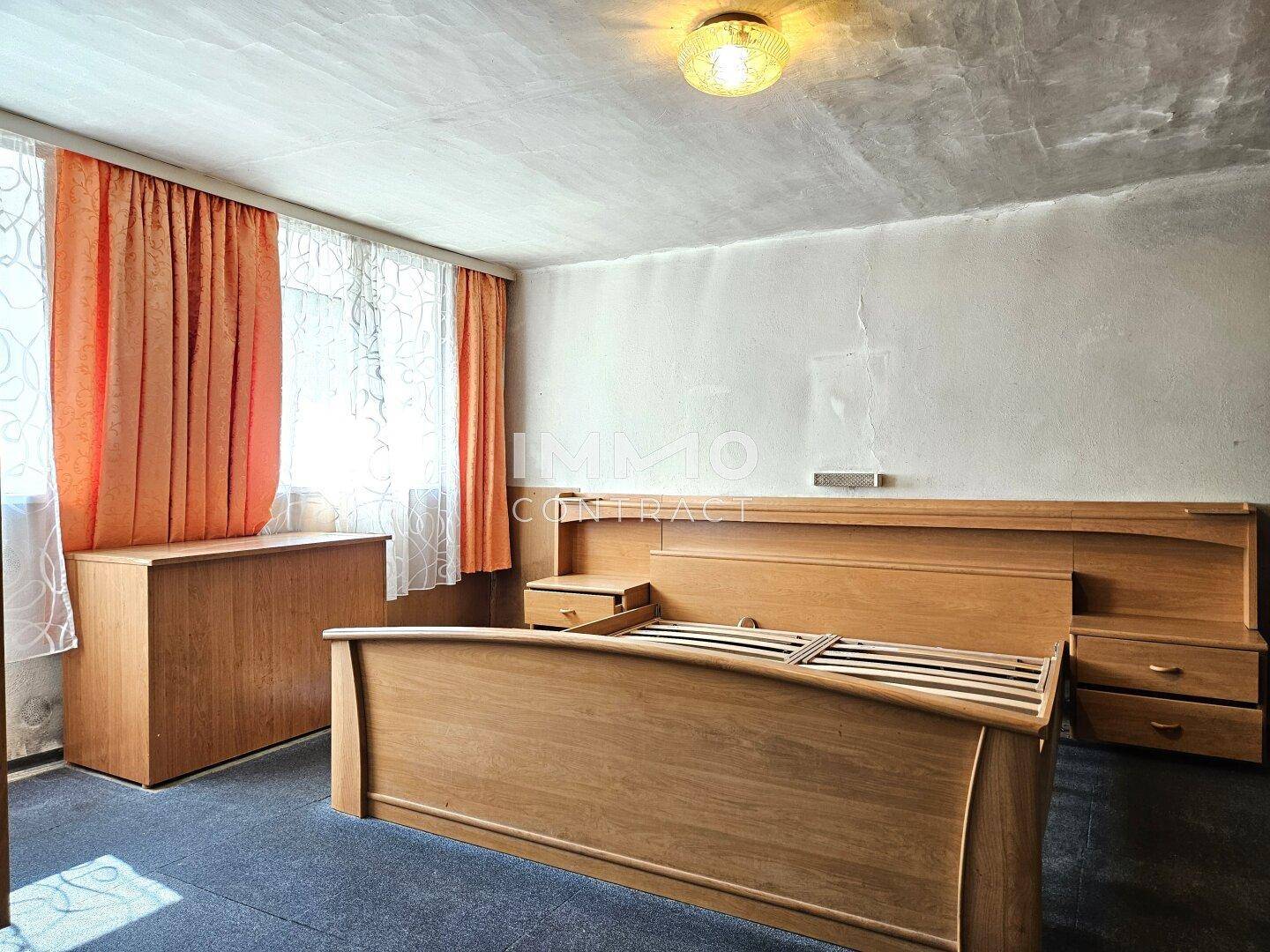 Schlafzimmer mit Holzbettrahmen, Nachttischen und Fenster mit Vorhängen.