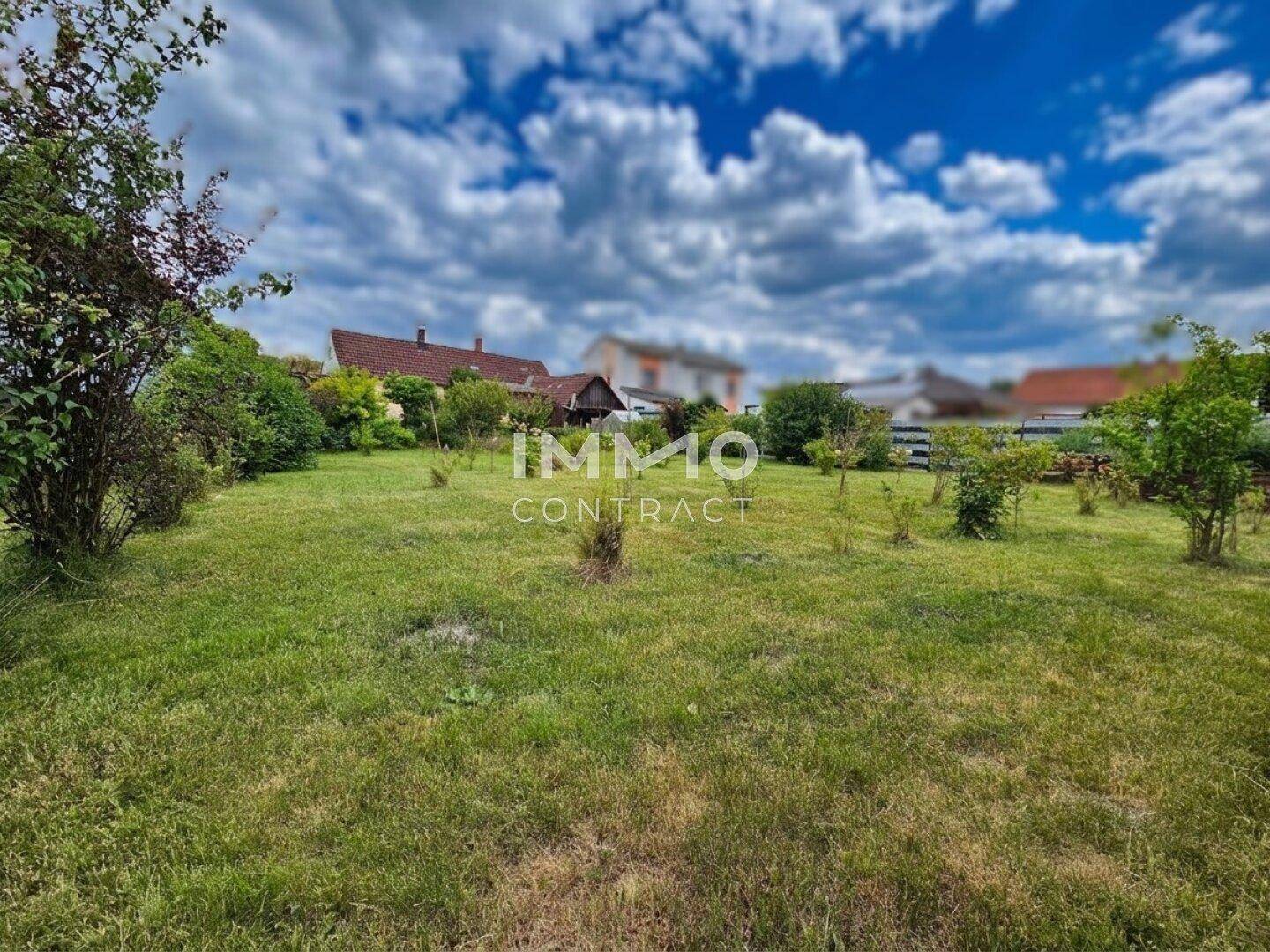 Großer Garten mit Rasenfläche und Blick auf umliegende Häuser unter bewölktem Himmel.
