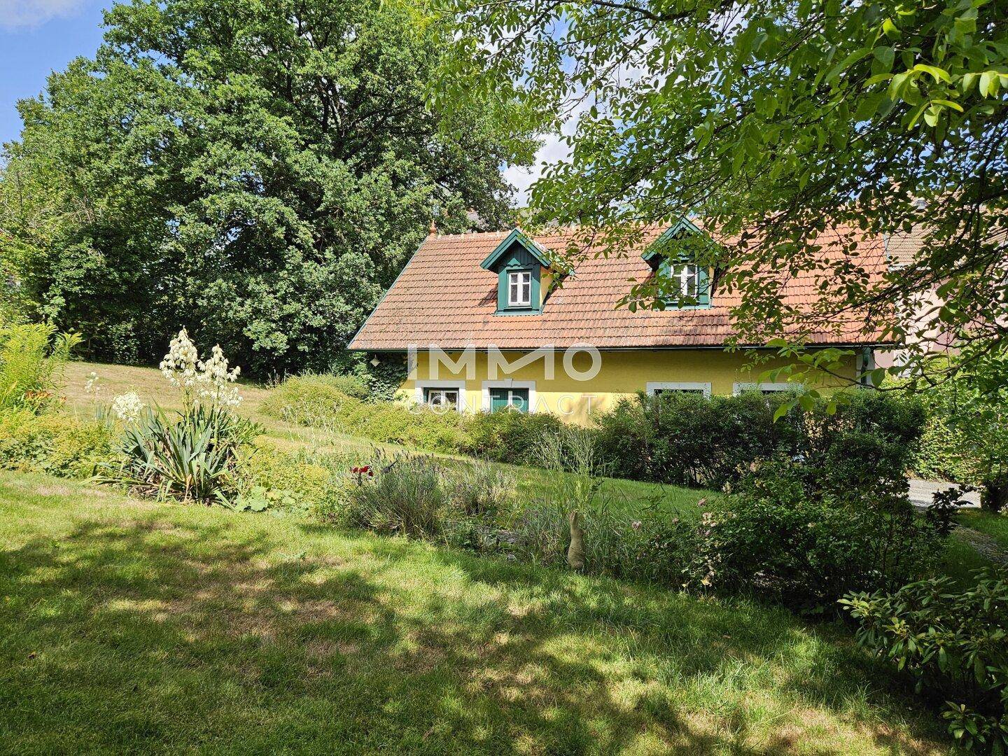 Das gelbe Haus ist eingebettet in eine weitläufige grüne Landschaft mit großen Bäumen und einem gepflegten Rasen.