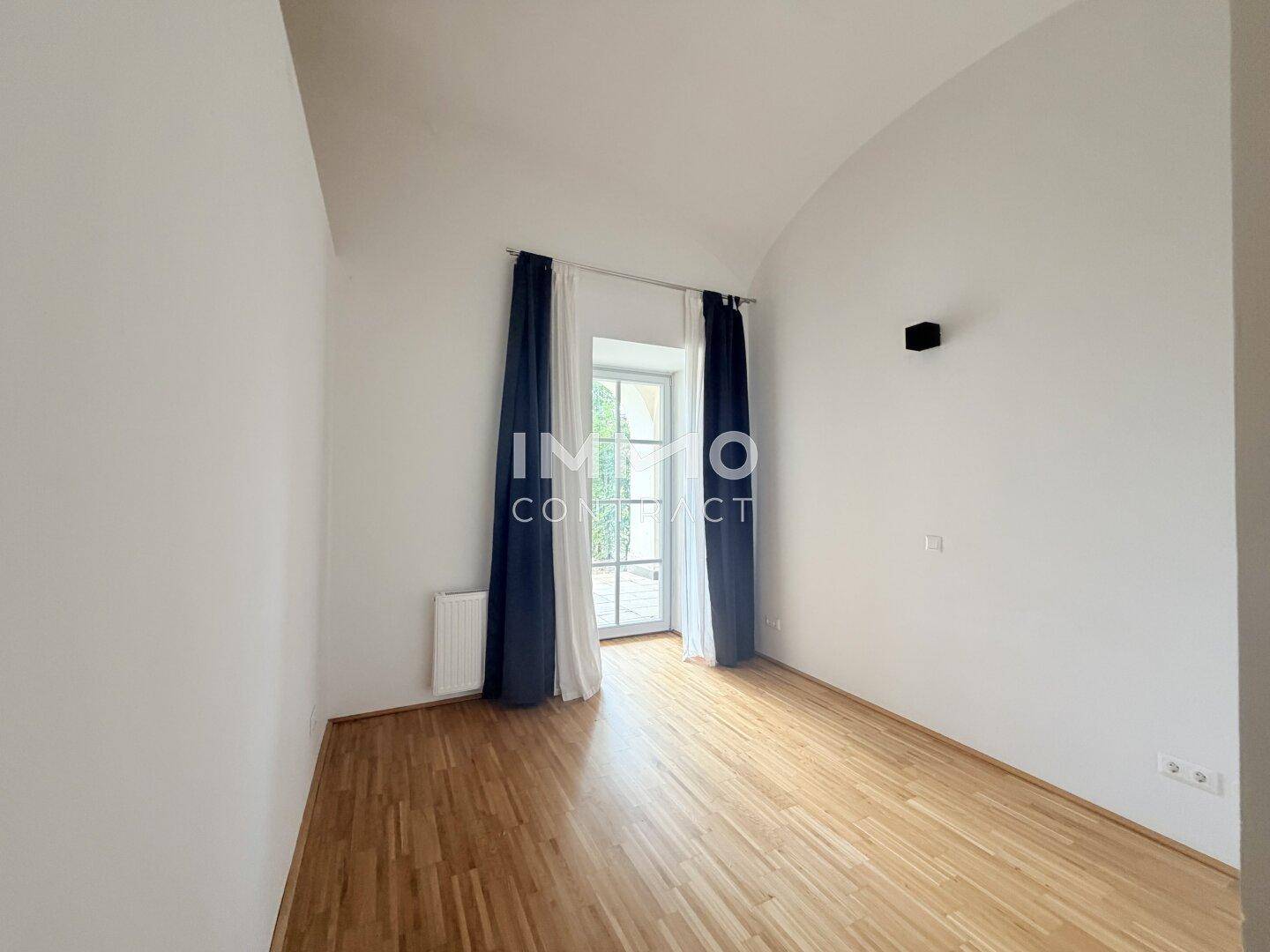 Helles Schlafzimmer mit Parkettboden, hohen Decken und Zugang zu einem französischen Balkon.