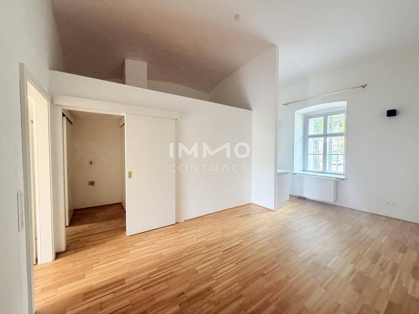 Heller Wohnraum mit Parkettboden, hohen Decken und einem großen Fenster für viel Tageslicht.
