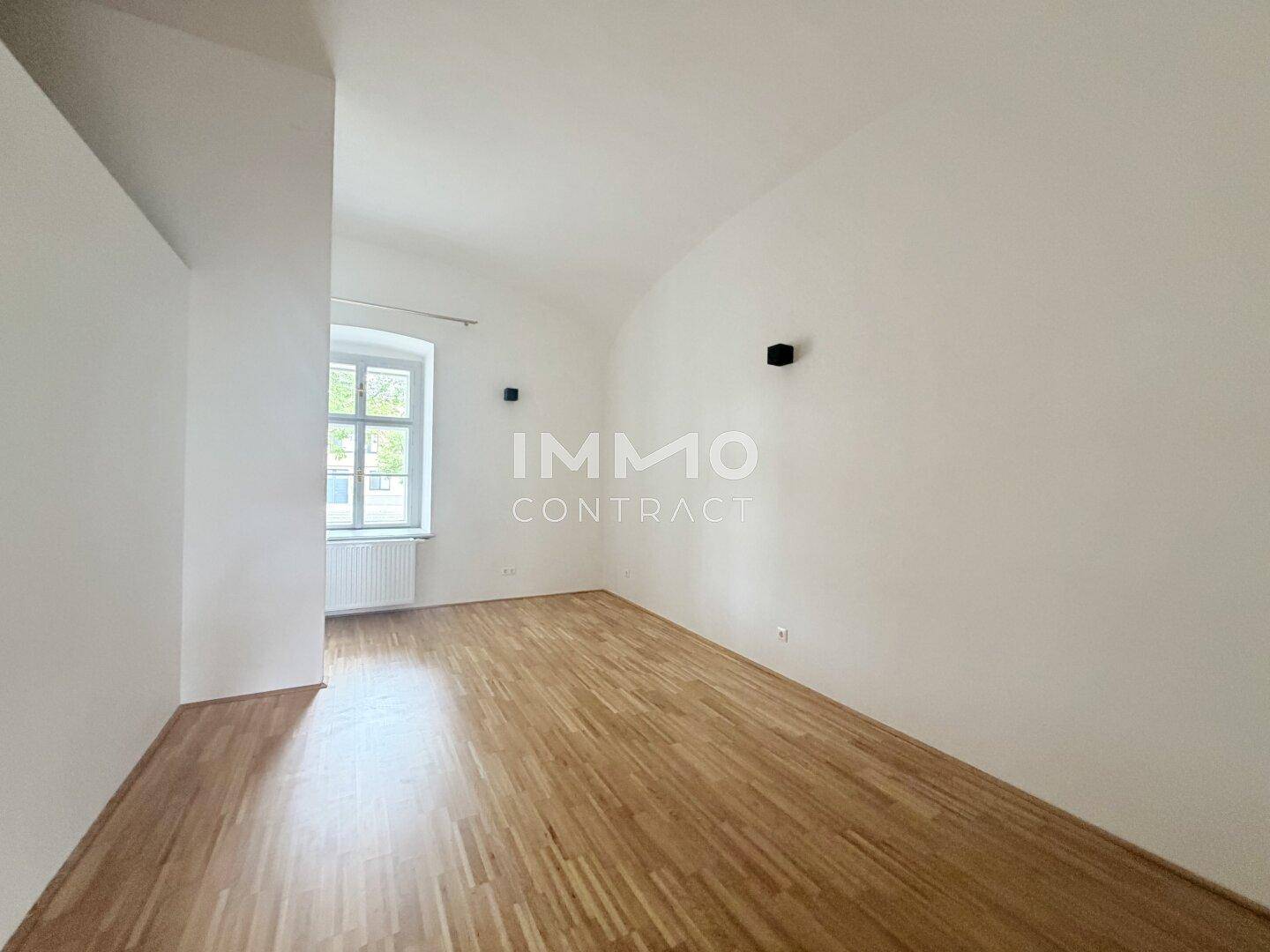 Geräumiges Schlafzimmer mit Parkettboden, hohen Decken und einem großen Fenster für viel Licht.