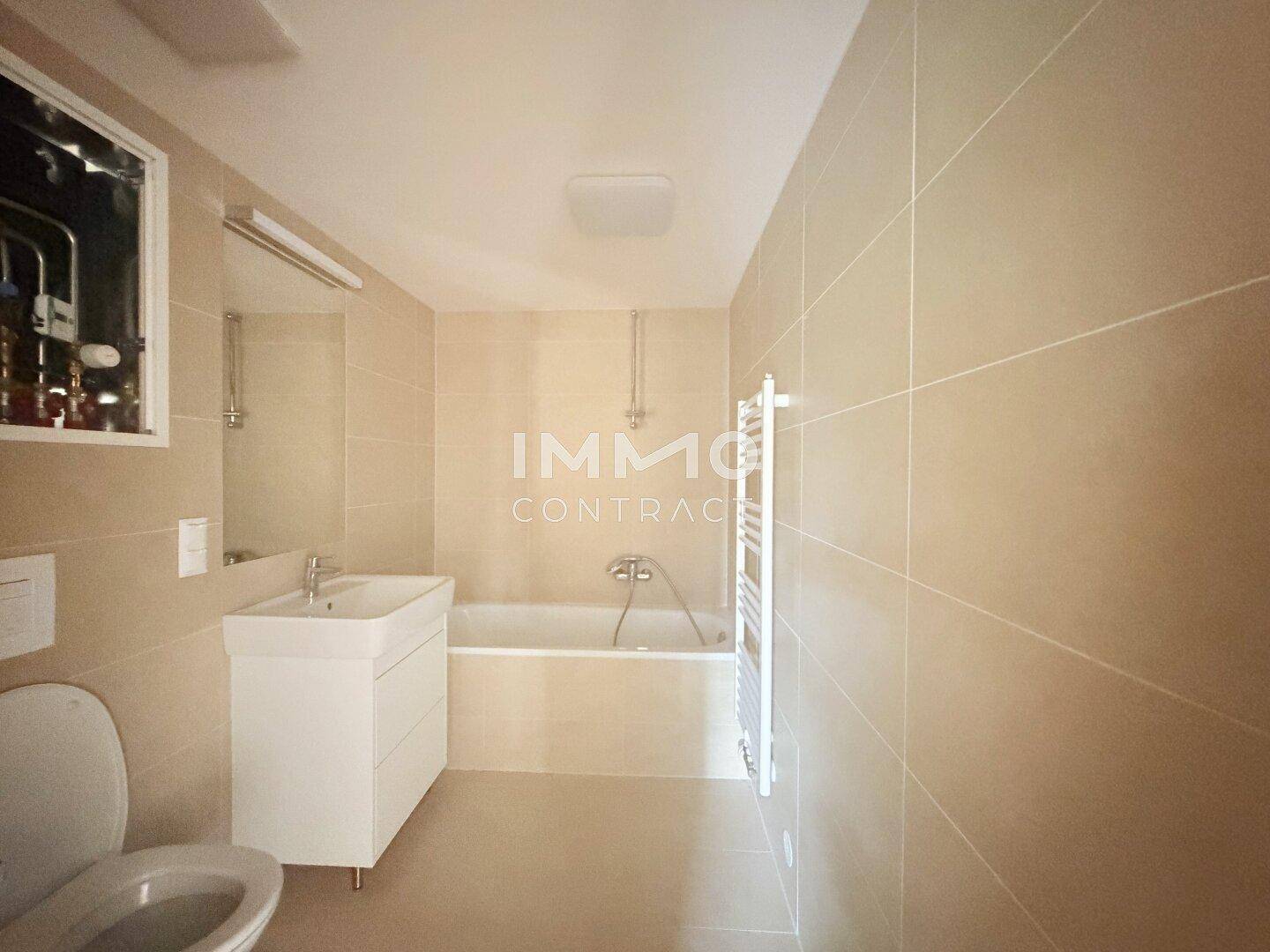 Modernes Badezimmer mit beigefarbenen Fliesen, Badewanne, Waschbecken und beheiztem Handtuchhalter.