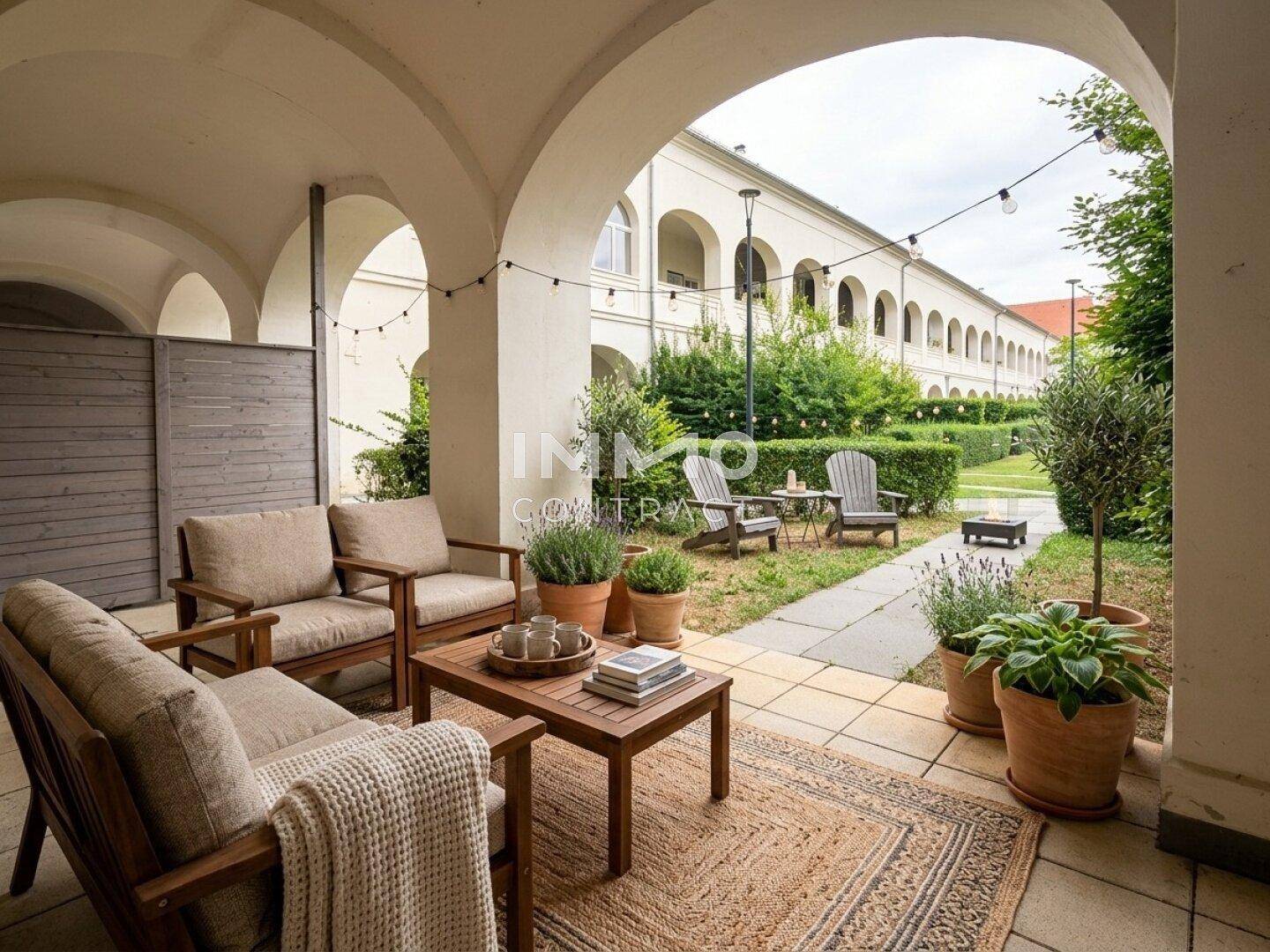Gemütliche Terrasse unter Arkaden mit bequemen Gartenmöbeln und Blick auf den grünen Innenhof.