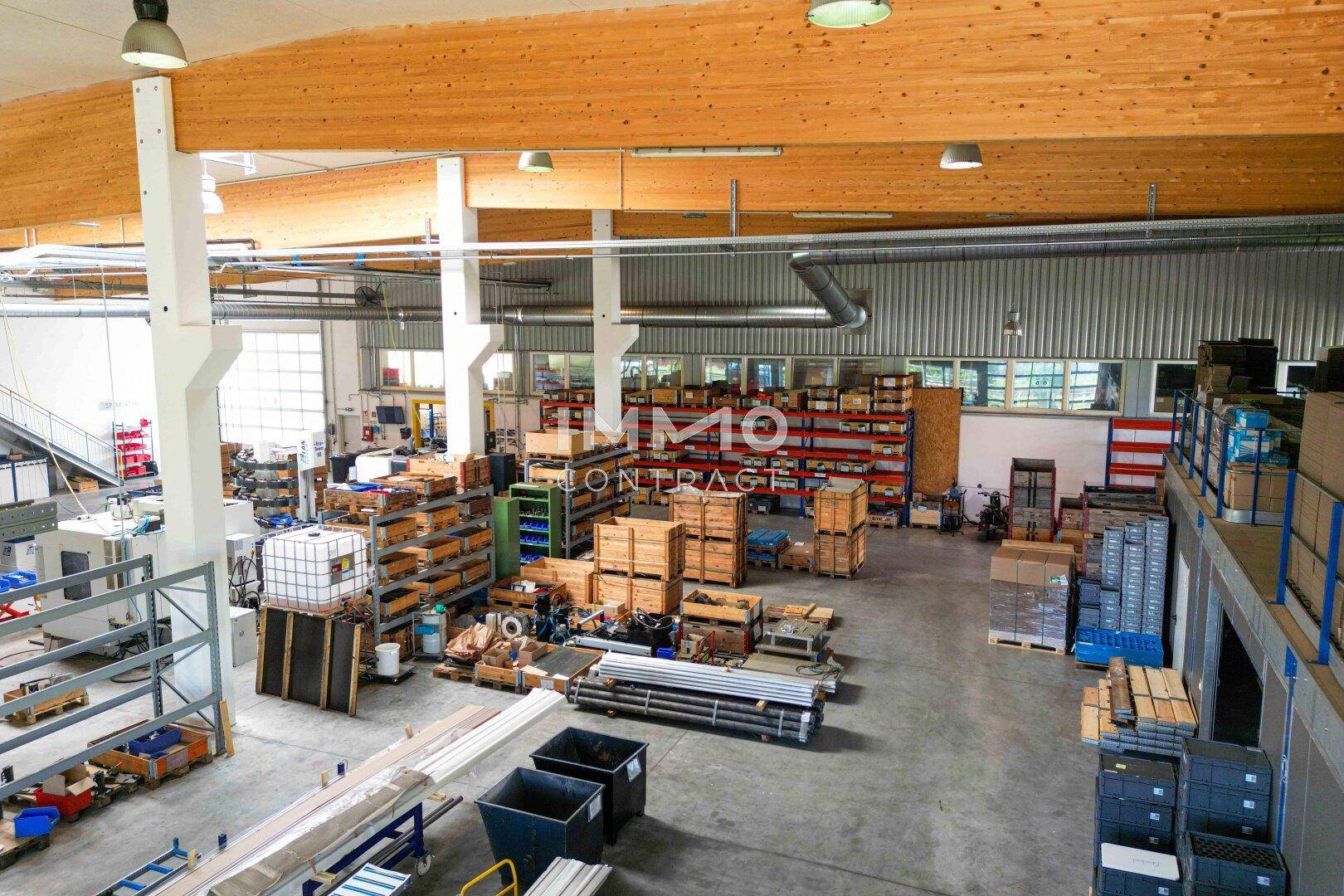 Geräumige Lagerhalle mit hohen Decken, sichtbaren Holzträgern und einem robusten Betonboden, gefüllt mit Regalen und Material.