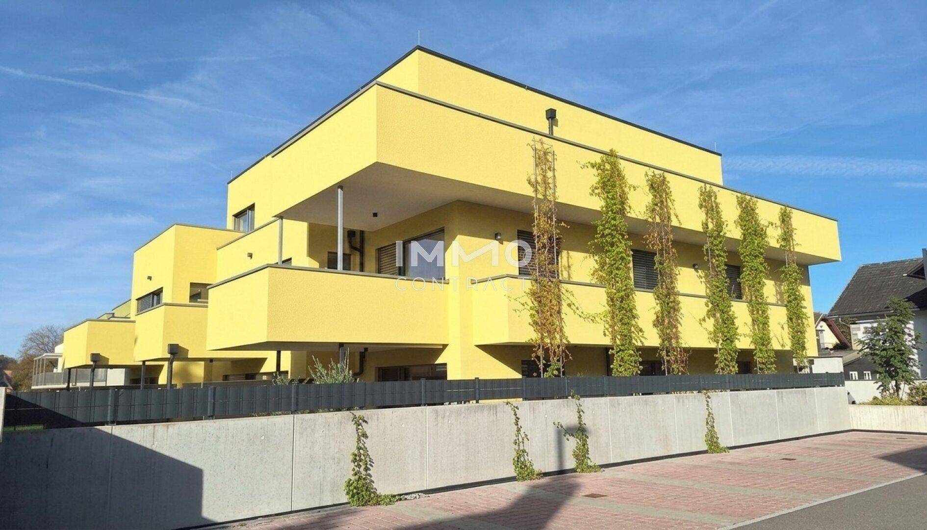Modernes gelbes Gebäude mit mehreren Balkonen und großen Fenstern unter blauem Himmel.