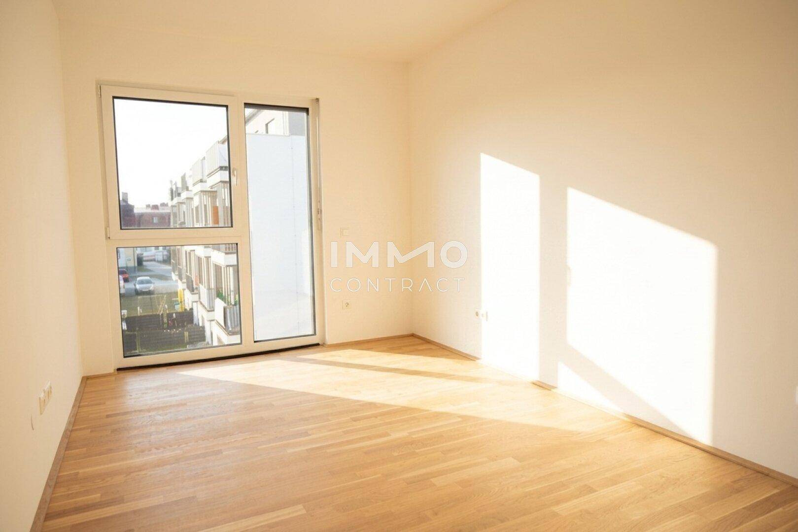 Helles Schlafzimmer mit Holzboden und großem Fenster, das viel Sonnenlicht hereinlässt.