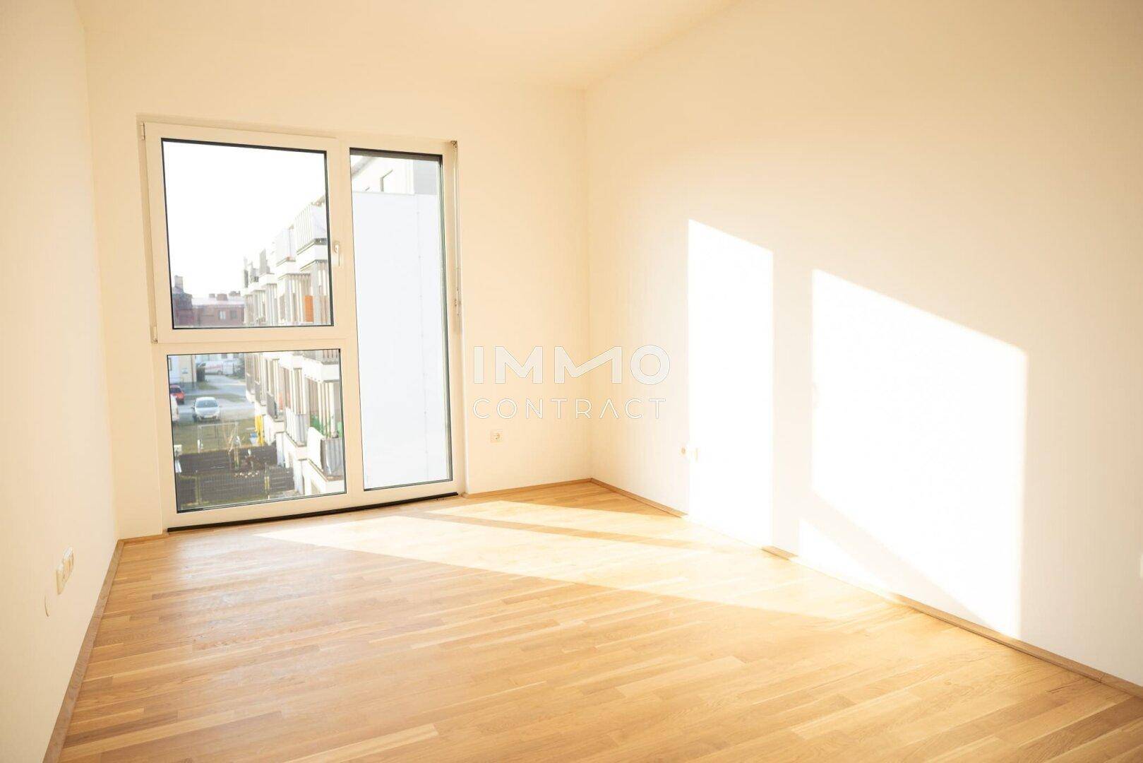 Lichtdurchfluteter Raum mit Holzboden und großem Fenster, das viel Sonnenlicht hereinlässt.