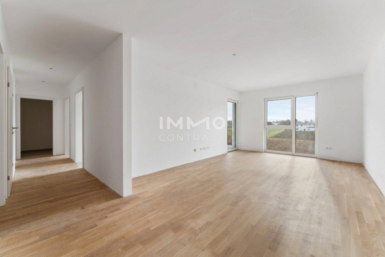 Geräumiger, heller Wohnbereich mit Holzboden und Zugang zu einem Balkon mit Weitblick.