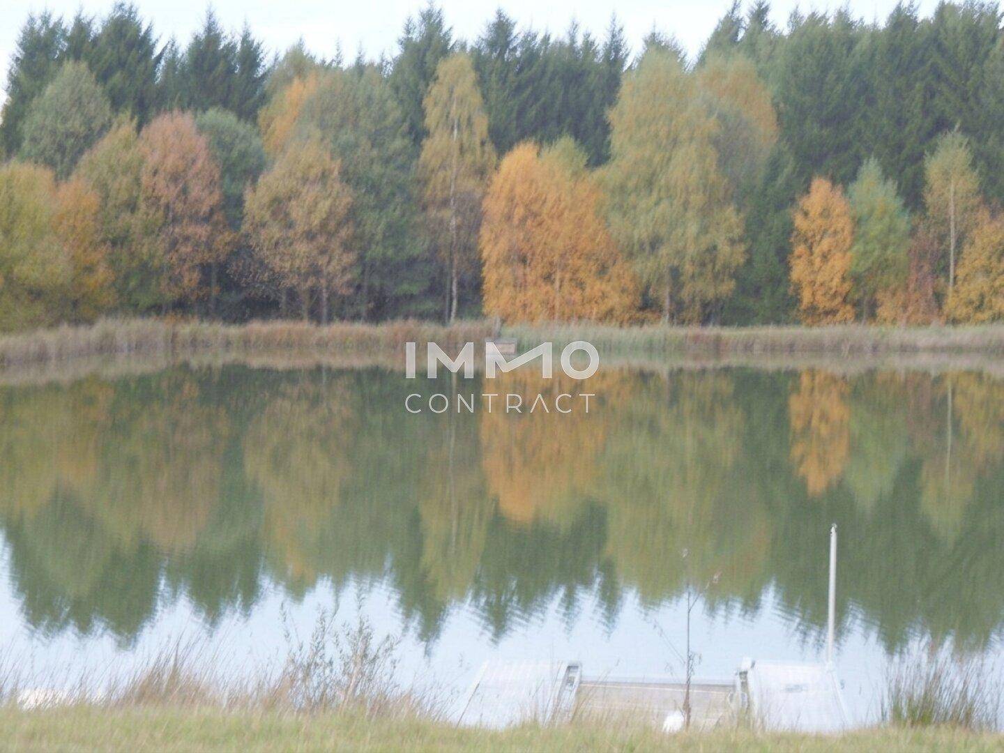 Ruhiger Teich mit Spiegelungen von herbstlichen Bäumen am Ufer unter einem bewölkten Himmel.