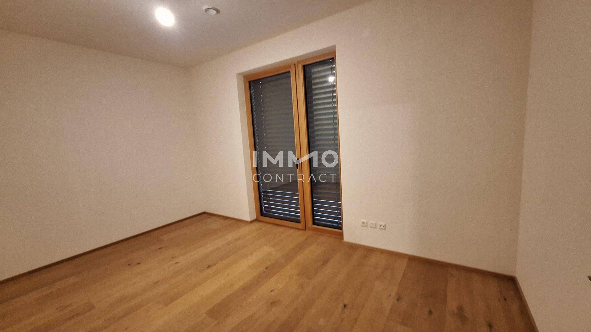 Helles Zimmer mit Holzboden und großem Fenster mit Jalousien, ideal als Schlaf- oder Arbeitszimmer.