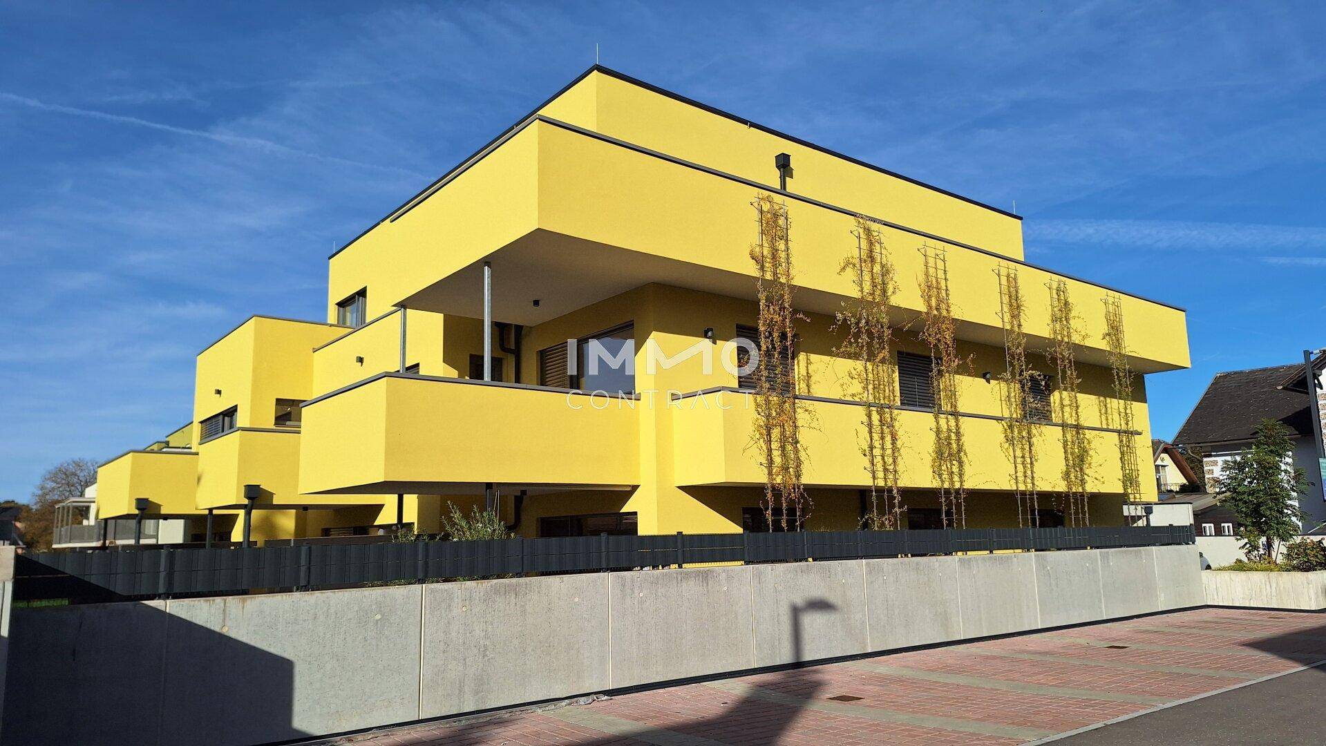 Modernes, gelbes Mehrfamilienhaus mit mehreren Balkonen und klarer Architektur unter blauem Himmel.
