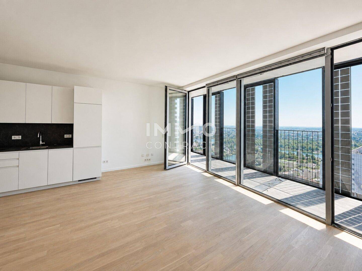 Offener Wohnbereich mit integrierter Küchenzeile, Holzboden und Zugang zu einem Balkon mit Stadtblick.