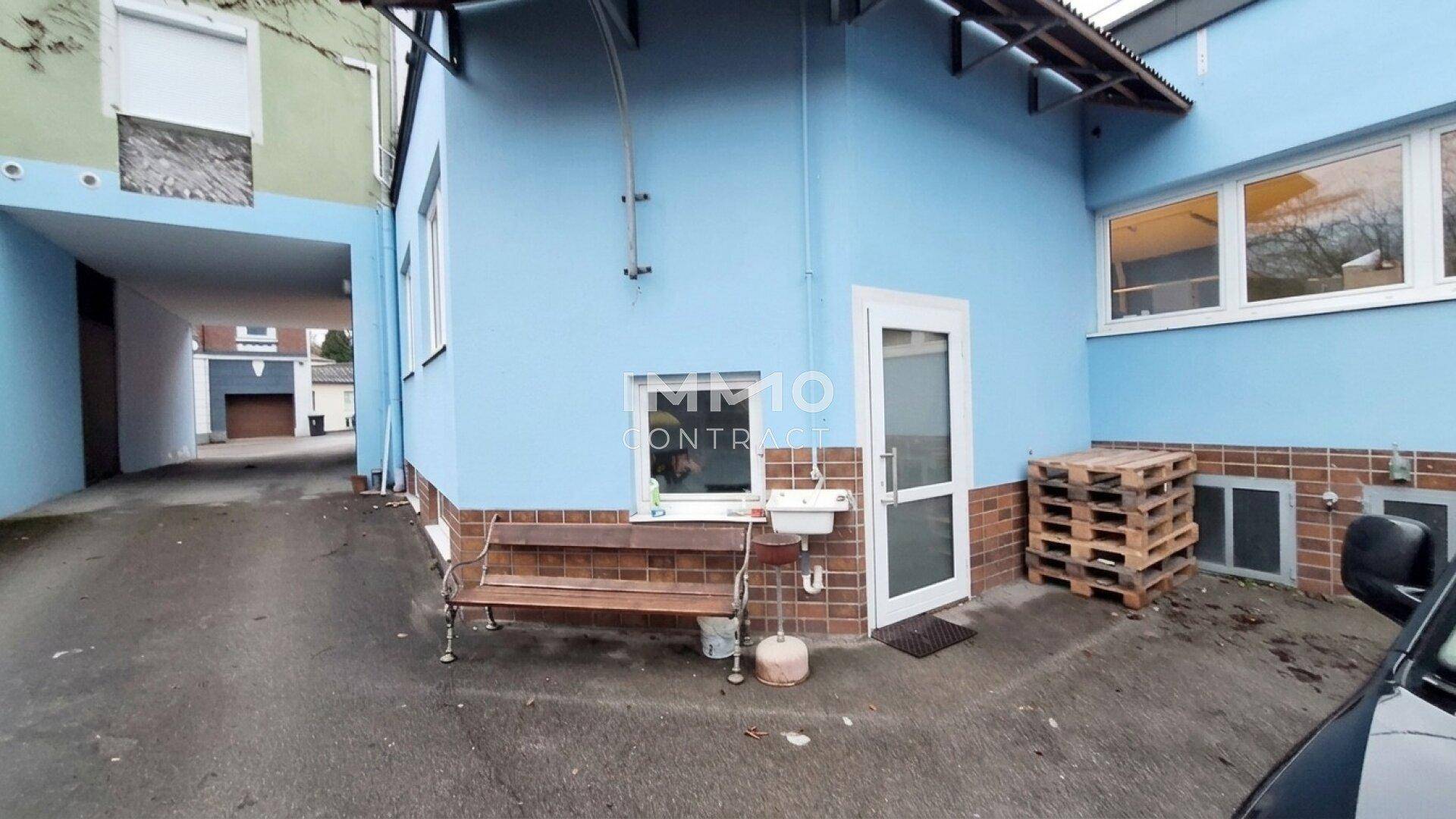 Außenansicht des Gebäudes mit blauer Fassade, Eingangstür und einem kleinen Hofbereich.