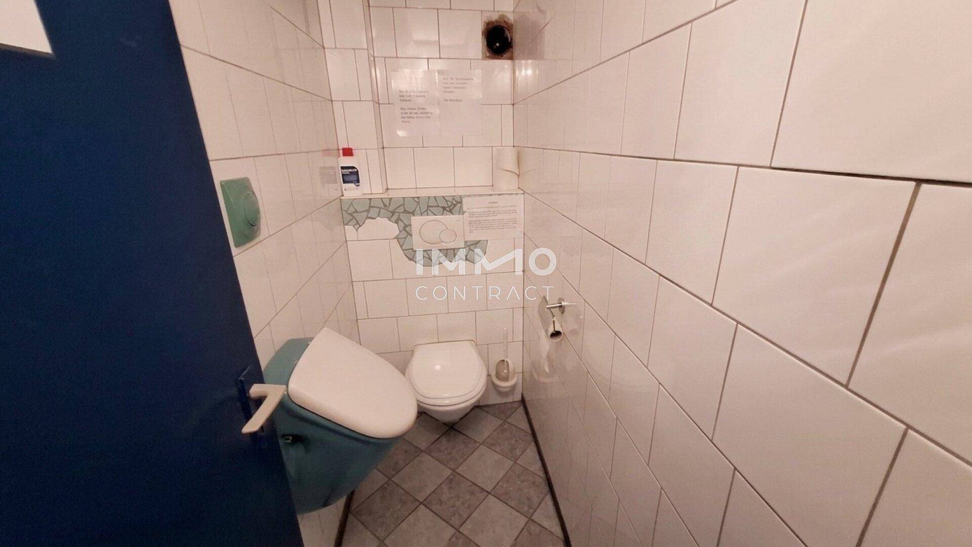 Kleiner Toilettenraum mit weißen Fliesen an den Wänden und einem Urinal.