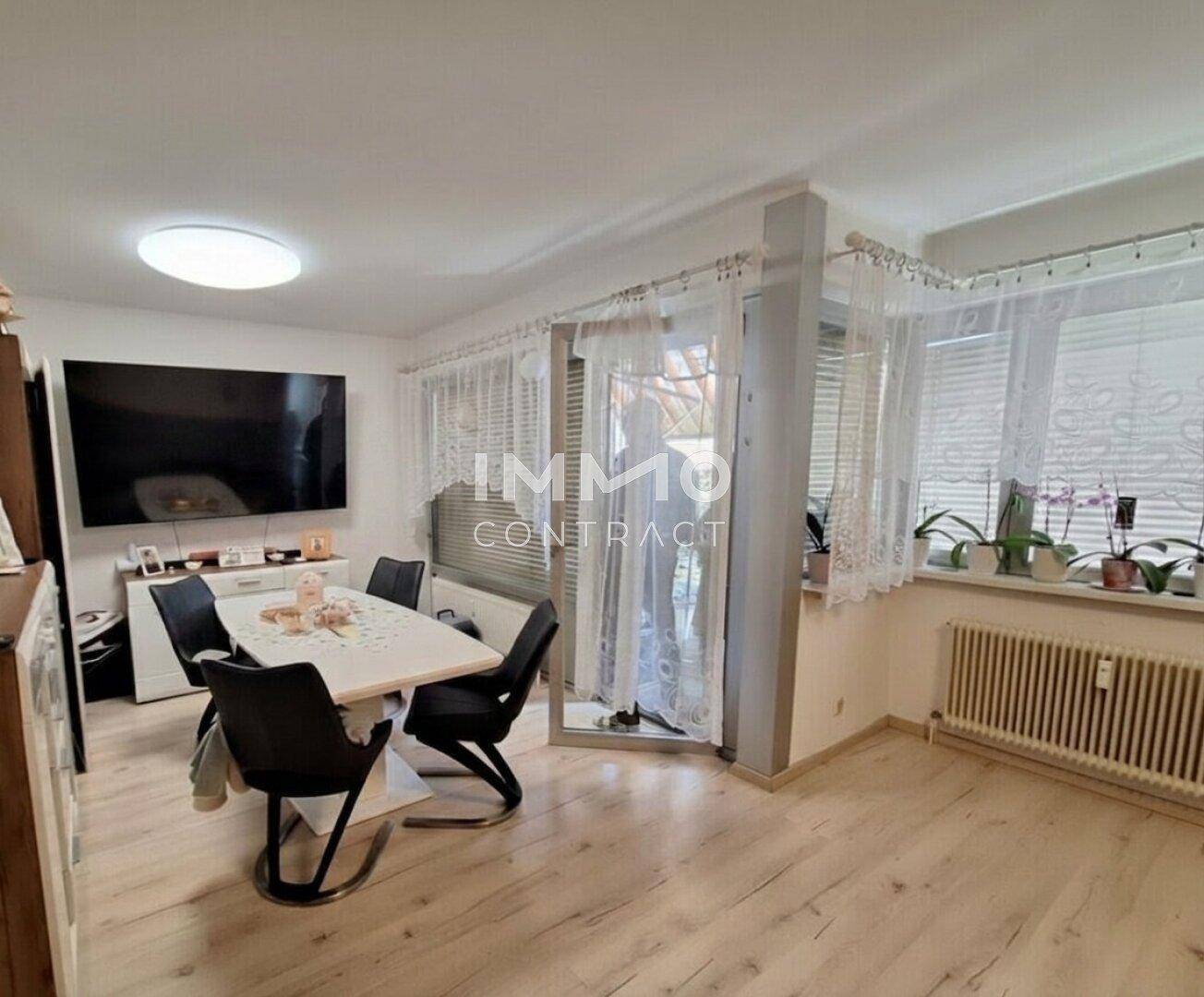 Heller Wohn- und Essbereich mit modernem Esstisch, großem Fernseher und Zugang zum Balkon.