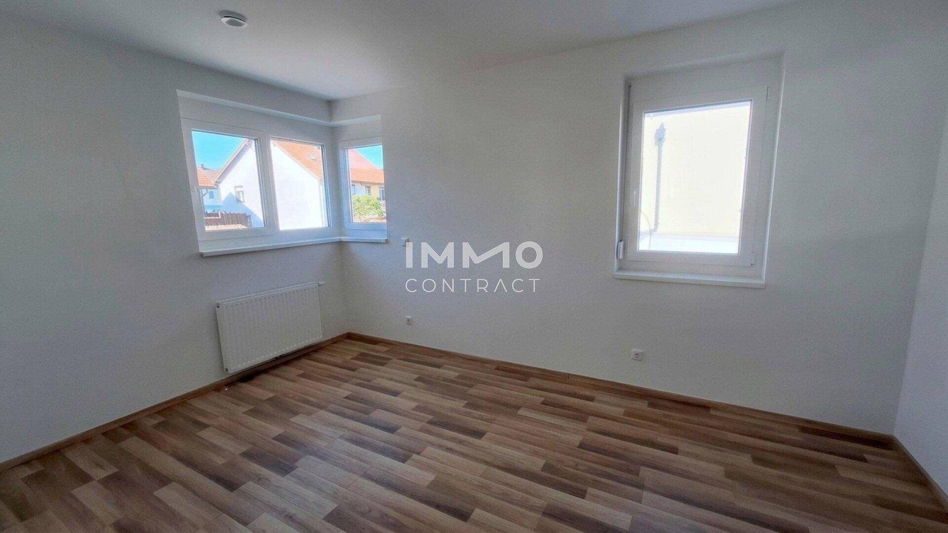 Heller, leerer Raum mit Laminatboden und zwei Fenstern, bereit zur individuellen Gestaltung.