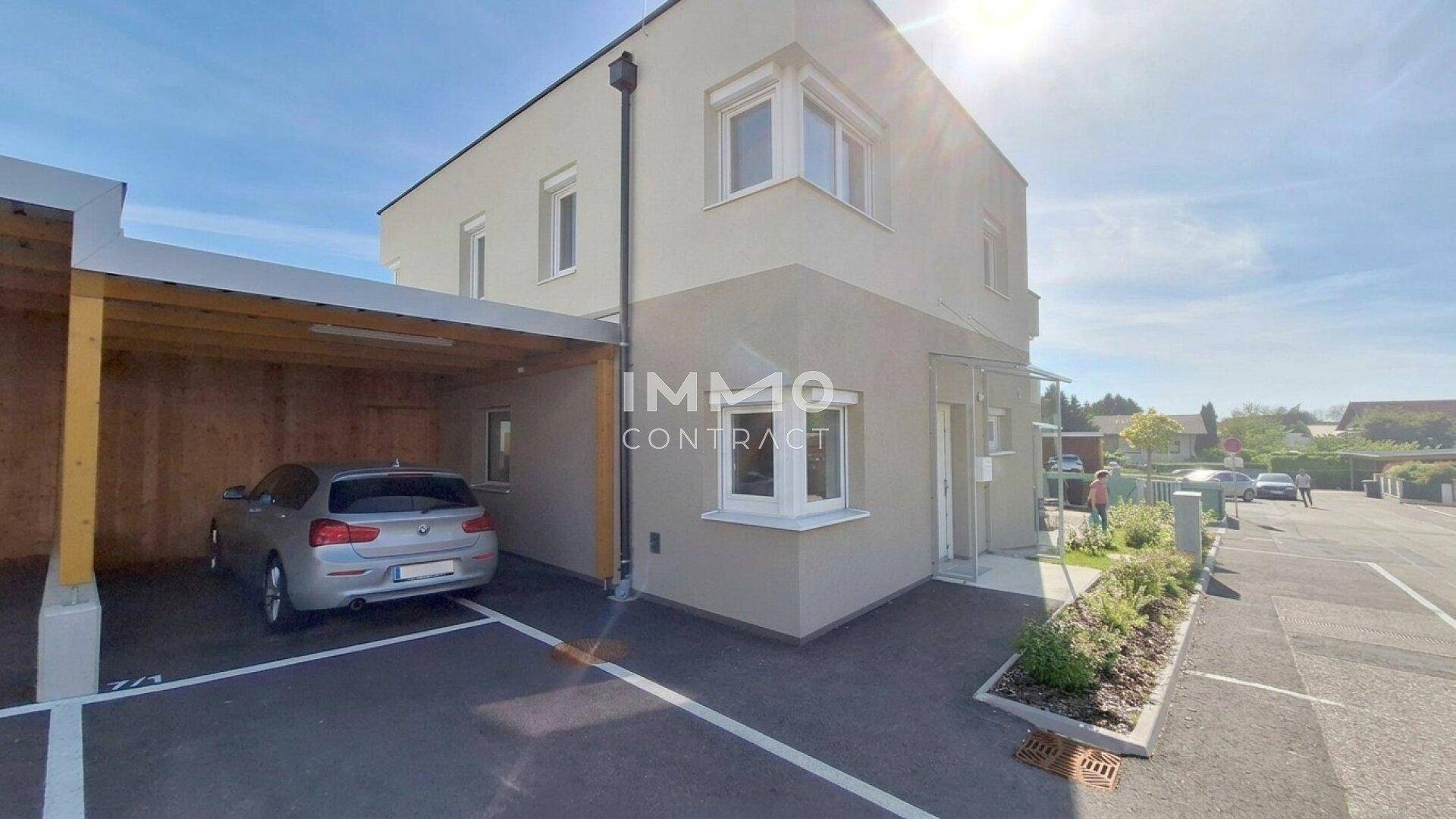 Moderne Hausfassade mit Carport und Außenstellplätzen unter strahlend blauem Himmel.