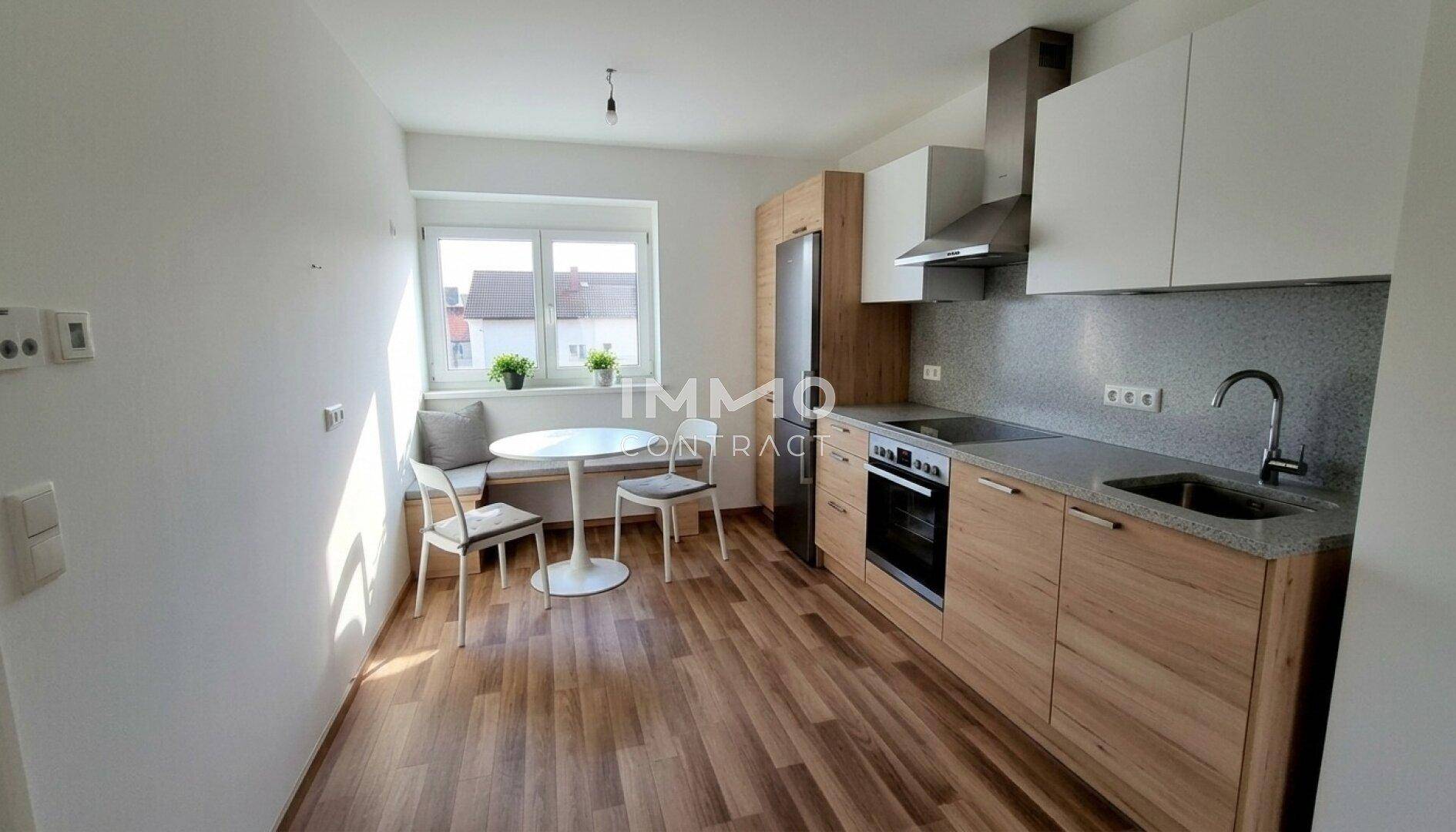 Moderne Einbauküche mit Holzelementen, Essbereich am Fenster und integrierten Geräten.
