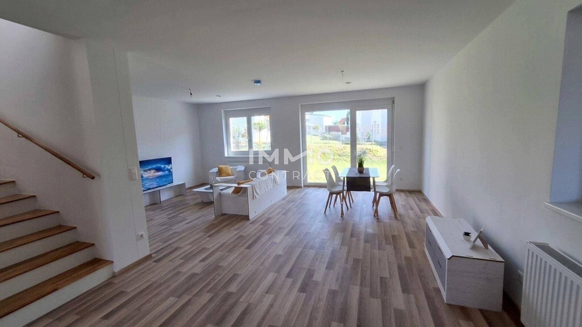 Geräumiger Wohn-Essbereich mit großen Fenstern, Laminatboden und Zugang zum Außenbereich.