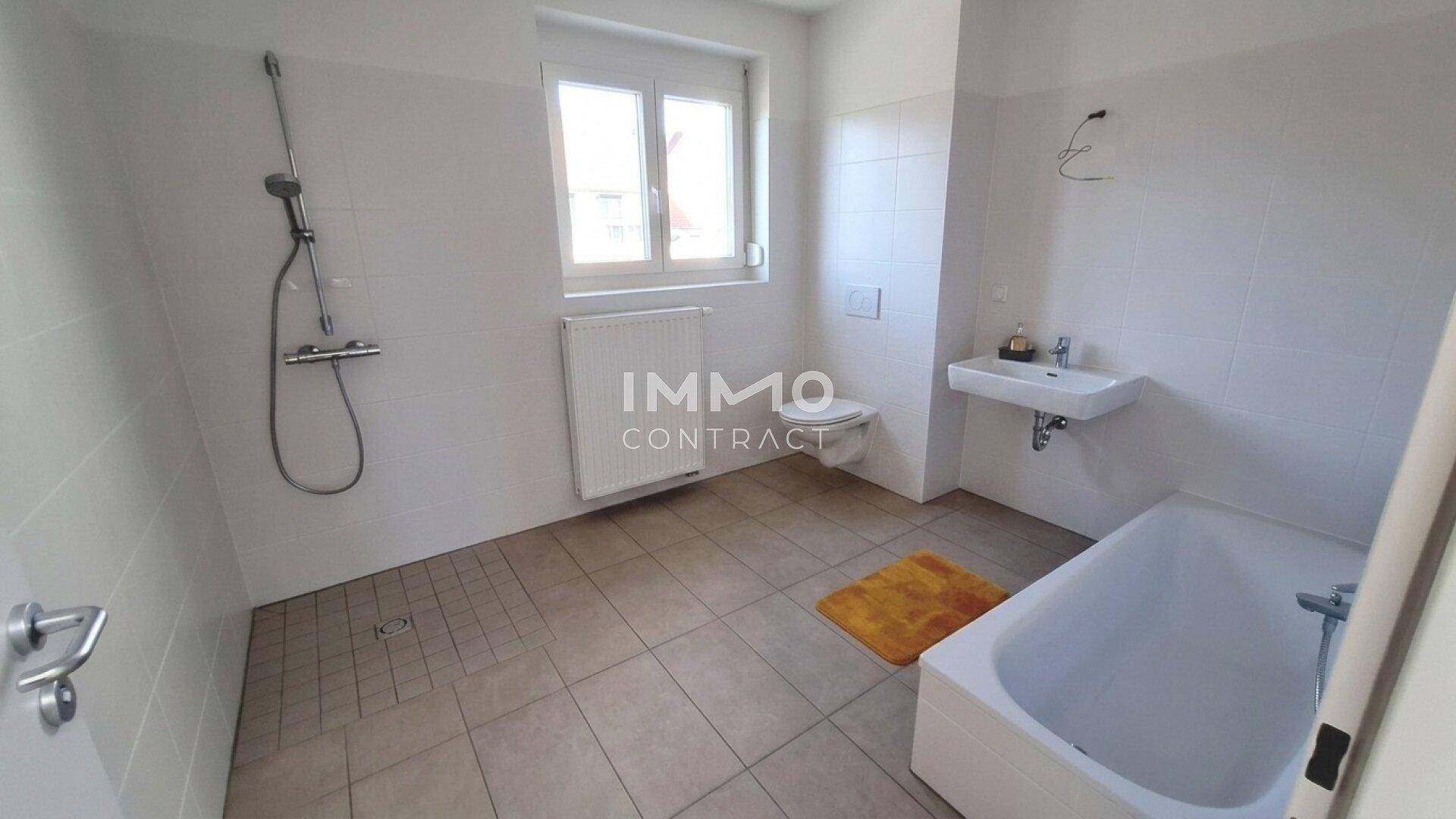 Helles Badezimmer mit Badewanne, Dusche, WC, Waschbecken und Fenster.