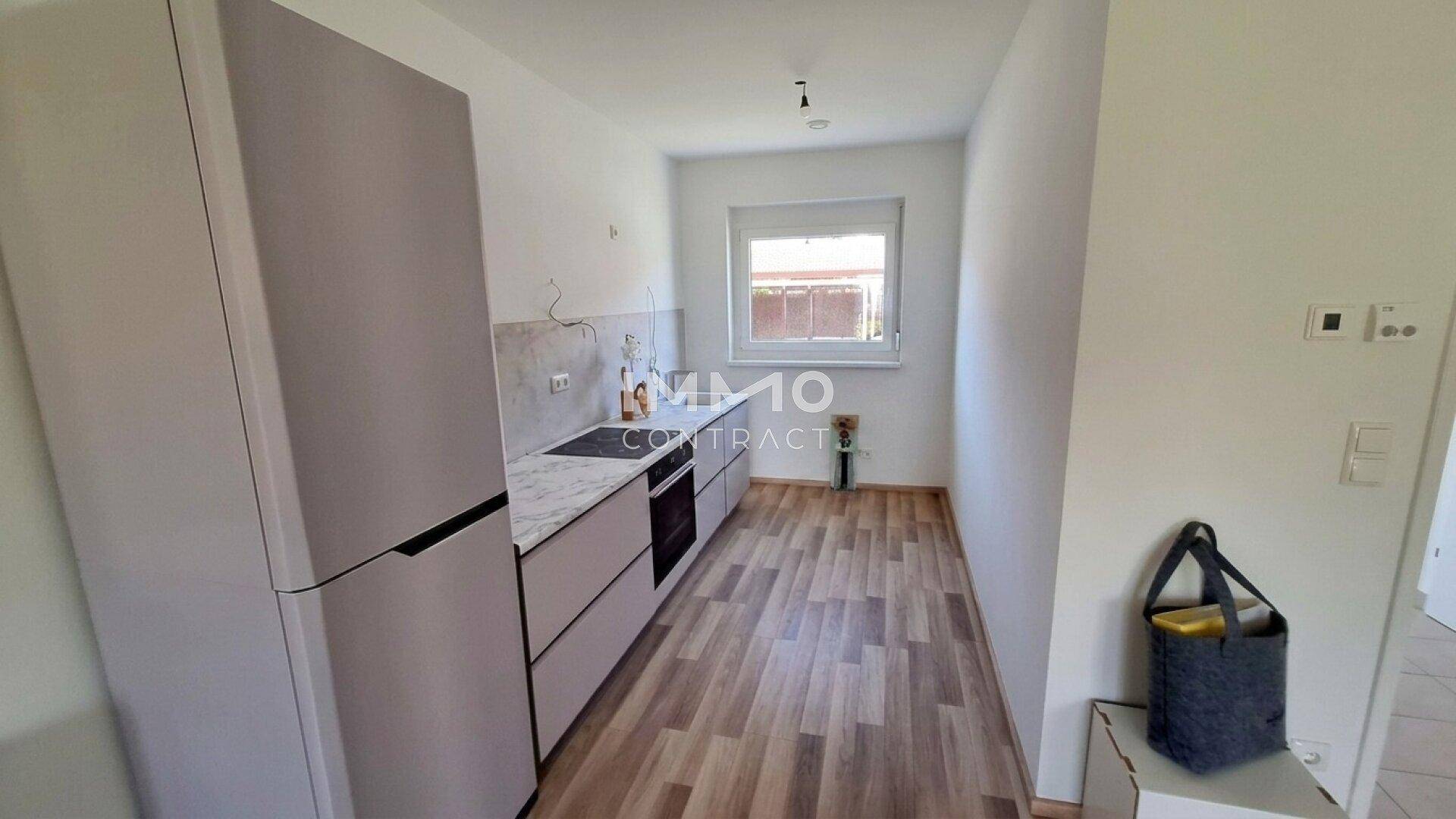 Moderne Küche mit hellgrauen Schränken, integrierten Geräten und Fenster.
