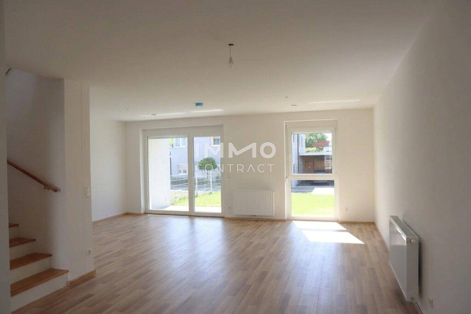 Helles Wohnzimmer mit großen Fenstern, Laminatboden und Zugang zum Garten.