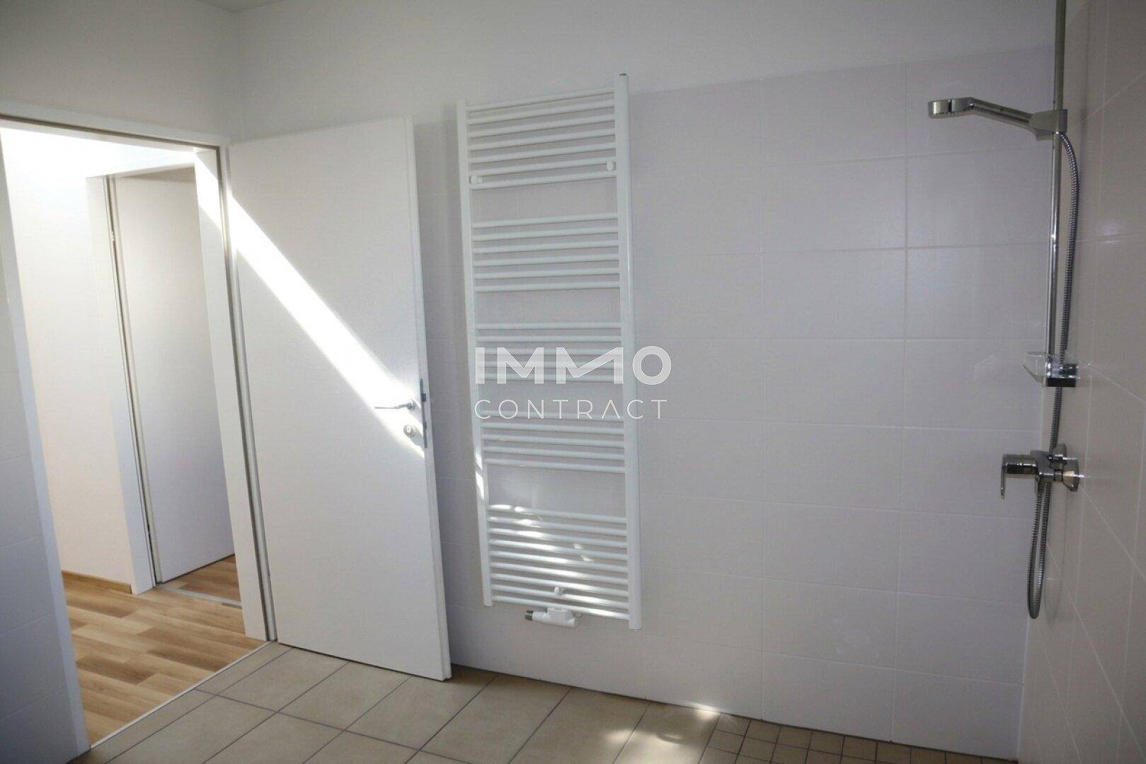 Badezimmer mit Duschbereich, beheiztem Handtuchhalter und hellen Wandfliesen.