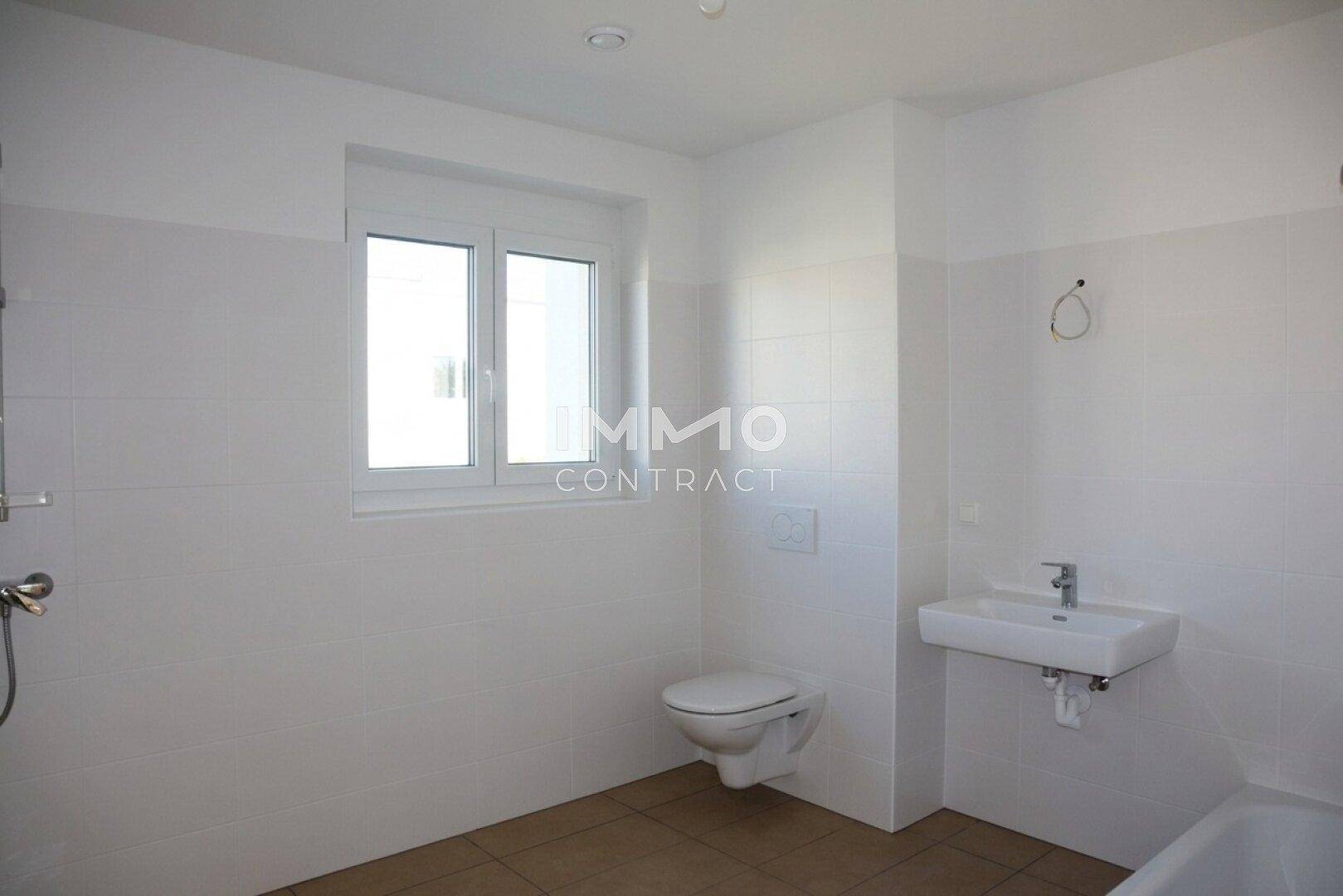 Modernes Badezimmer mit Fenster, Wand-WC, Waschbecken und hellen Fliesen.