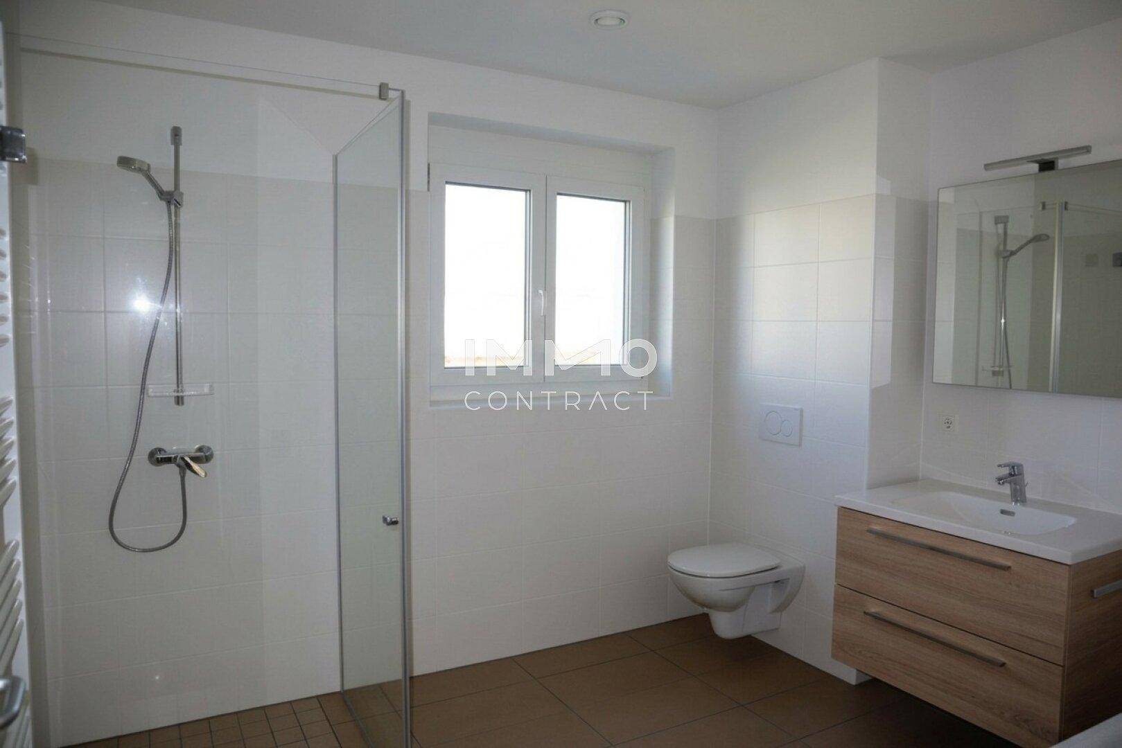 Helles Badezimmer mit ebenerdiger Dusche, wandhängendem WC und einem Fenster für Tageslicht.