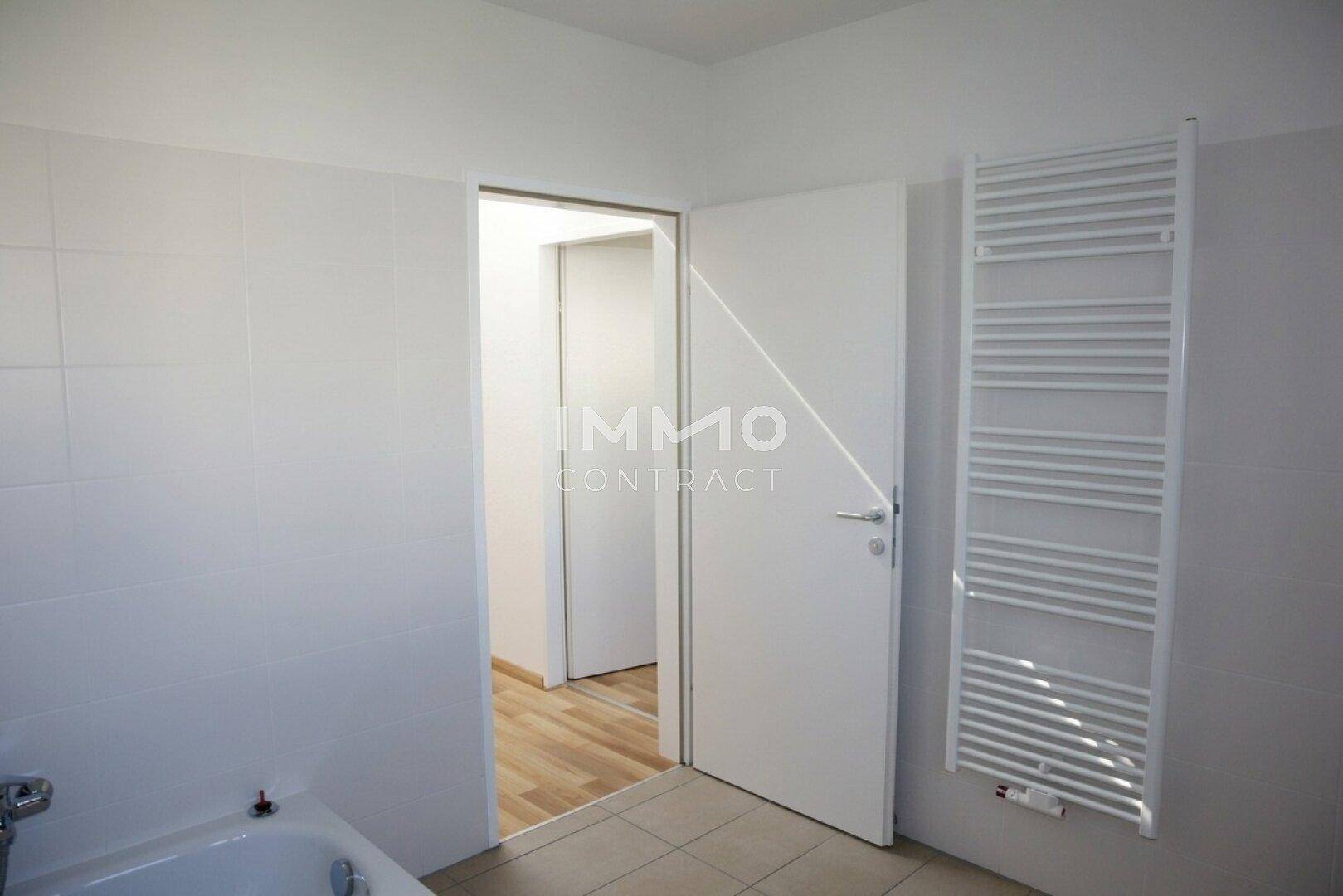 Badezimmer mit Badewanne, praktischem Handtuchheizkörper und Zugang zu einem weiteren Raum.