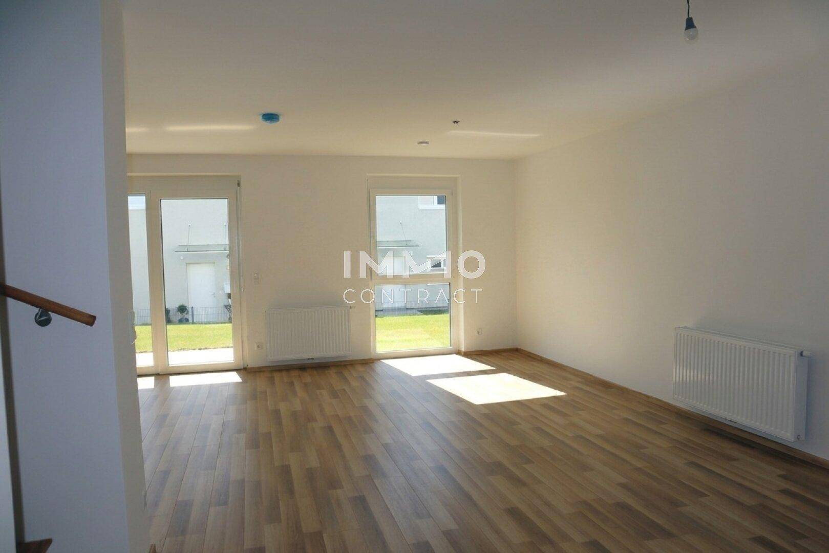 Helles Wohnzimmer mit Laminatboden und großen Fenstern mit Zugang zum Garten.