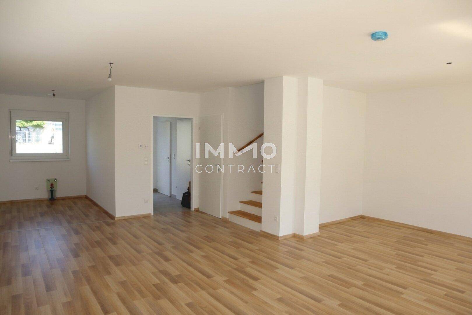 Geräumiges Wohnzimmer mit Laminatboden, weiß gestrichenen Wänden und Treppenaufgang.