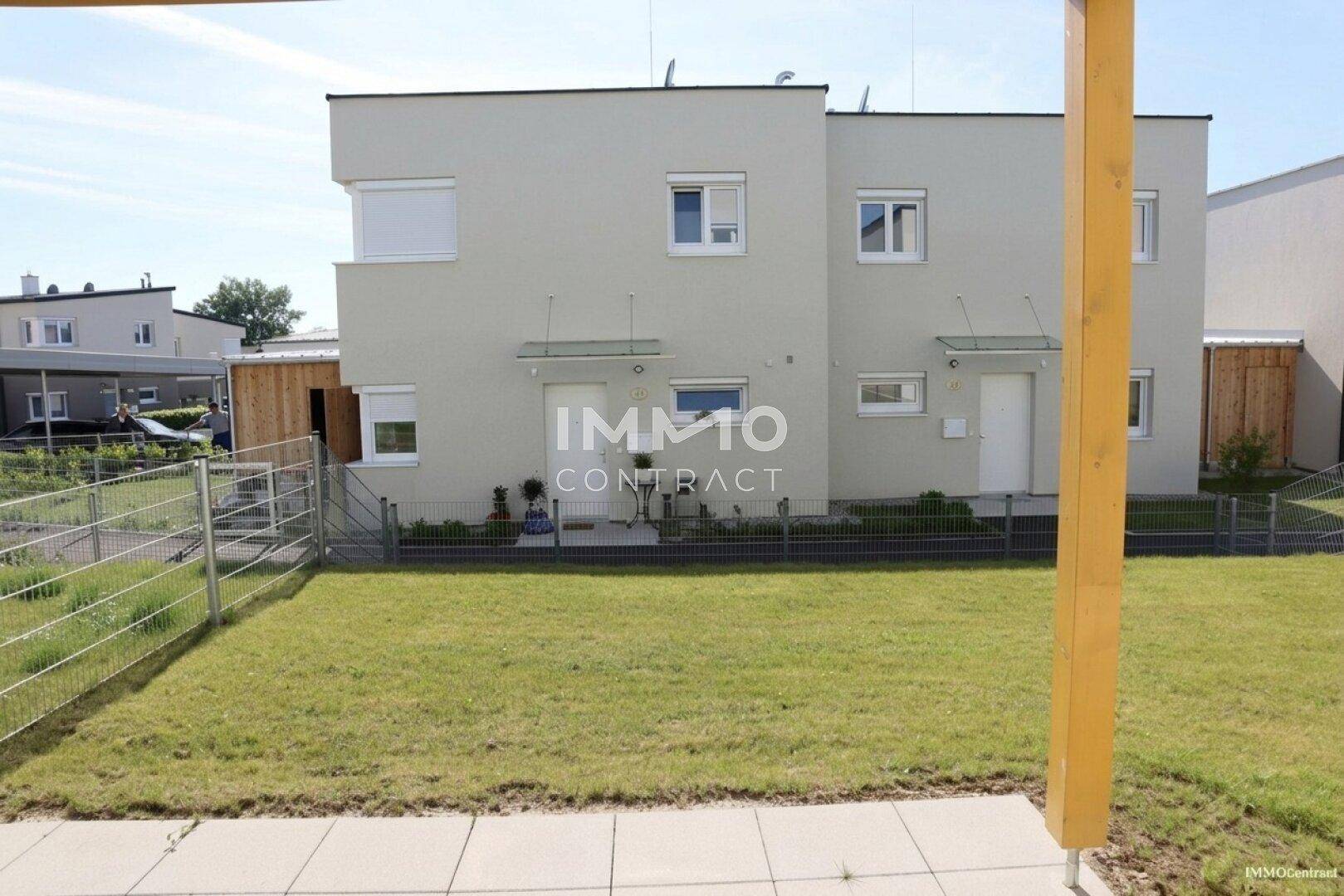 Gepflegter Gartenbereich hinter zwei modernen Reihenhäusern mit Rasenfläche und Zaun.