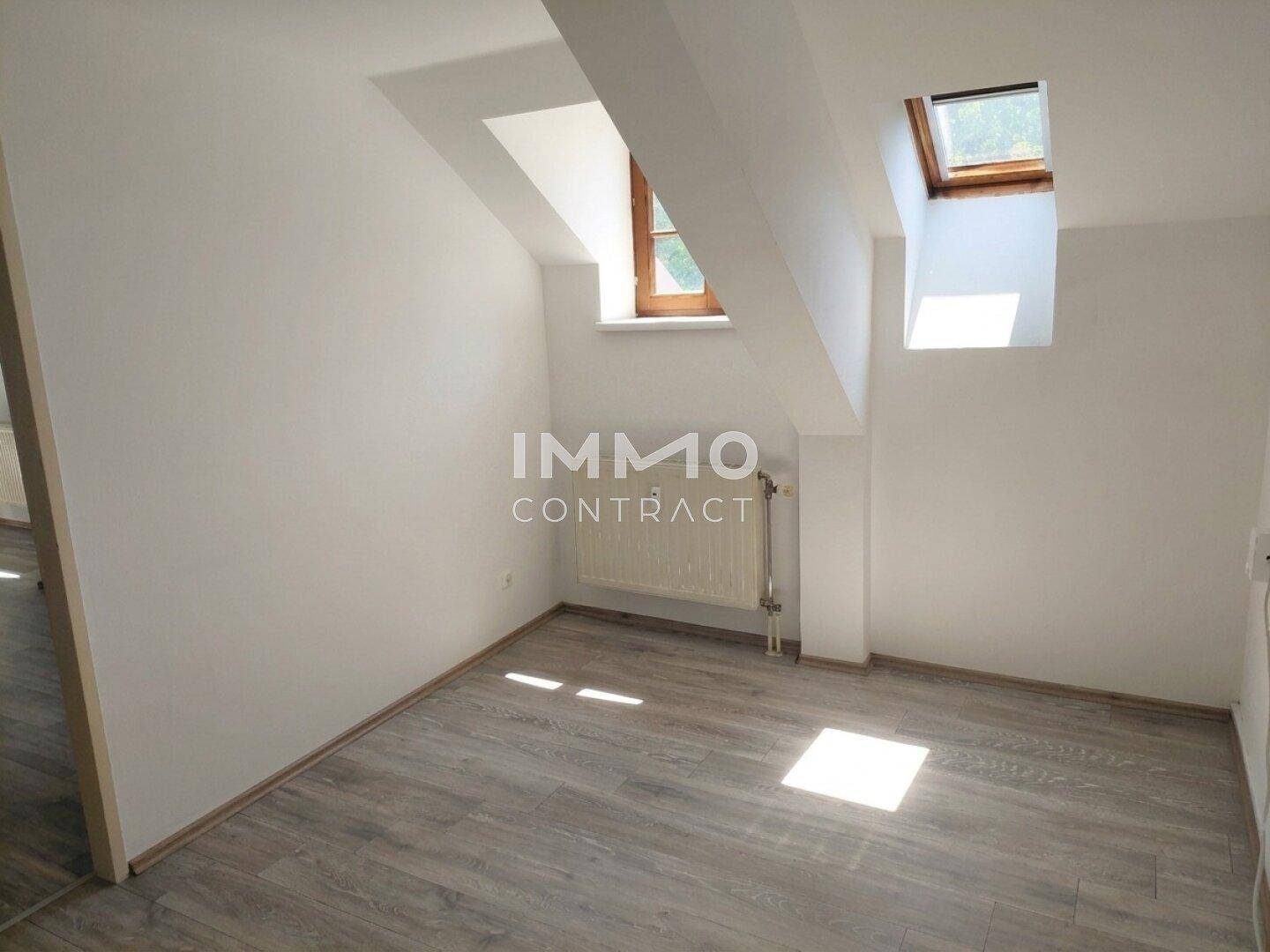 Helles Zimmer im Dachgeschoss mit Laminatboden, Dachfenstern und Heizkörper.