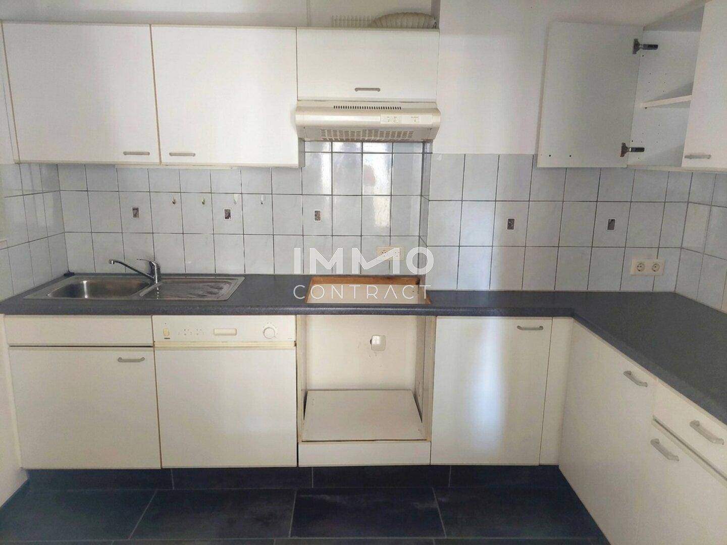 Funktionale Einbauküche mit weißen Schränken, dunkler Arbeitsplatte und Spülbecken.