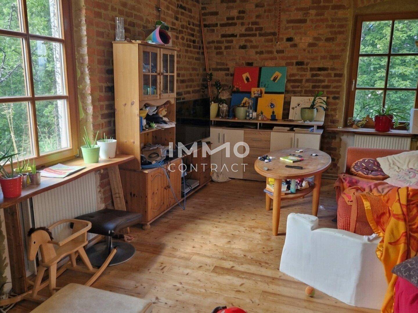 Gemütliches Wohnzimmer mit freiliegenden Ziegelwänden, Holzboden und Blick ins Grüne durch große Fenster.