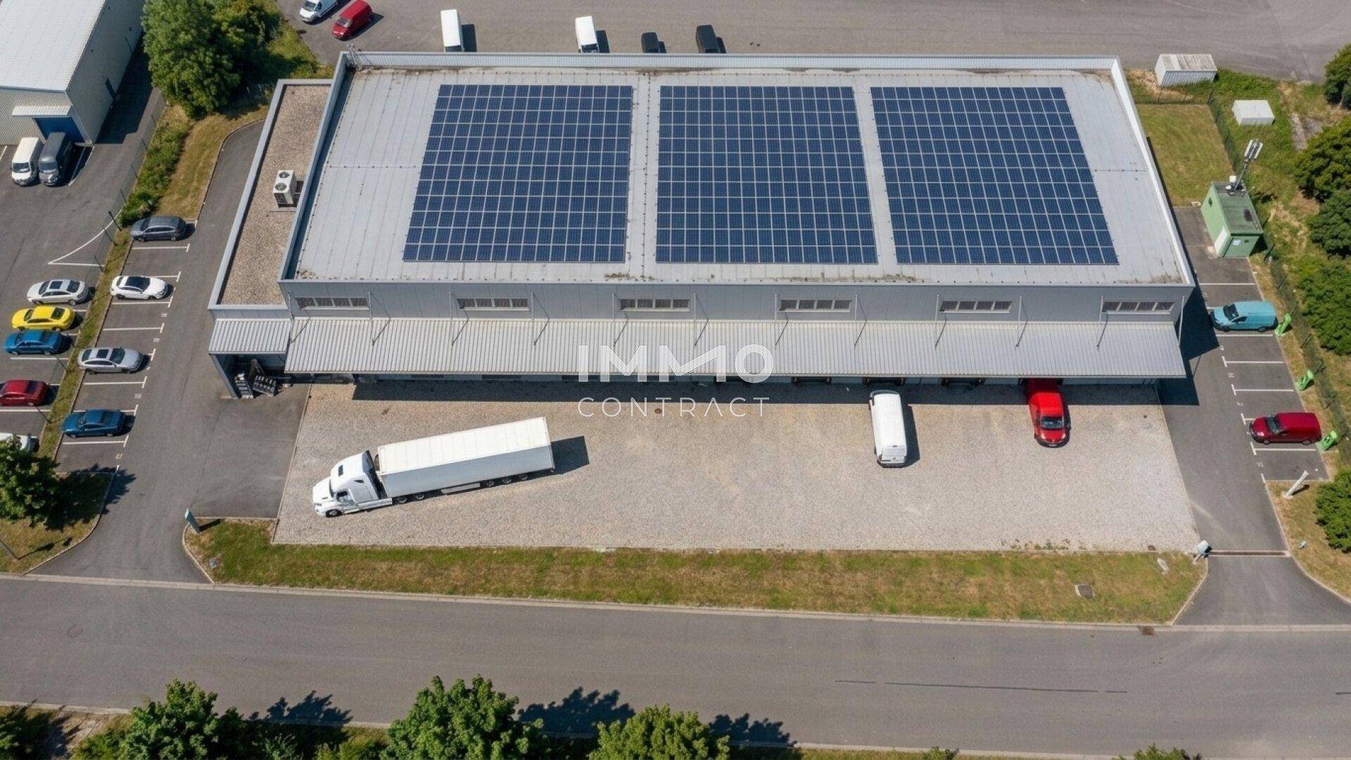 Luftaufnahme eines modernen Gewerbegebäudes mit Photovoltaikanlage auf dem Dach und großem Parkplatz.