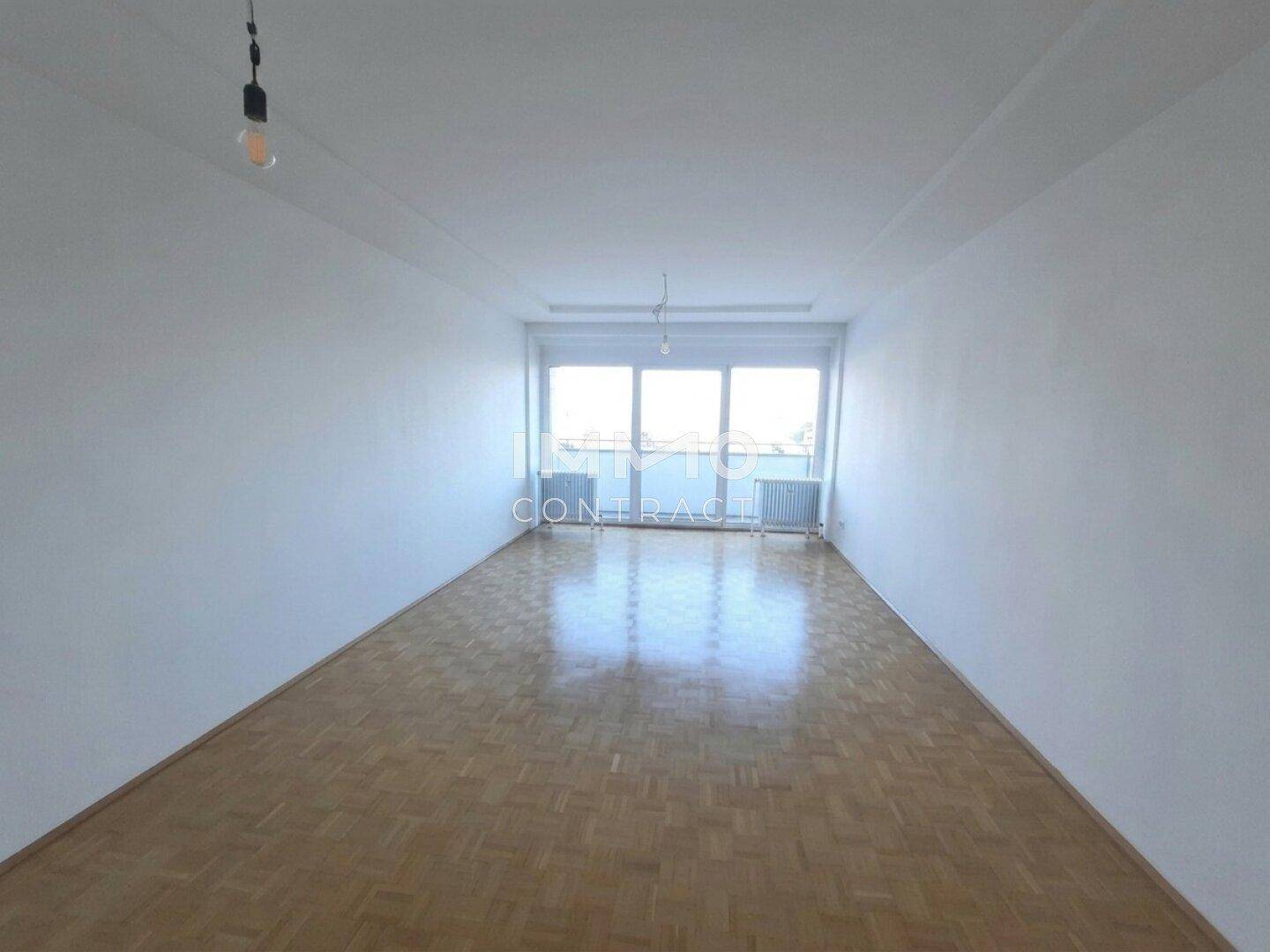 Weitläufiges Wohnzimmer mit glänzendem Parkettboden und breiter Fensterfront für viel Helligkeit.