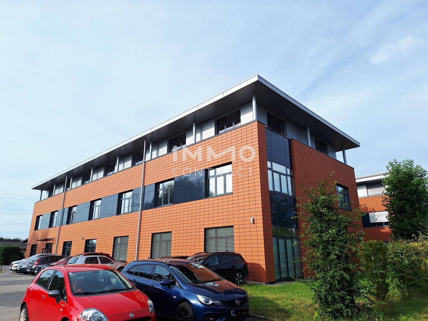 Ansicht des modernen Bürogebäudes mit orangefarbener Fassade und Parkplätzen im Vordergrund.
