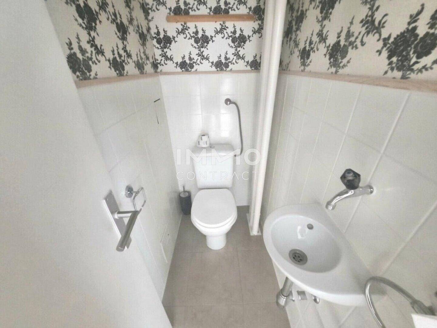 Separates WC mit Toilette, kleinem Waschbecken und auffälliger floraler Tapete.